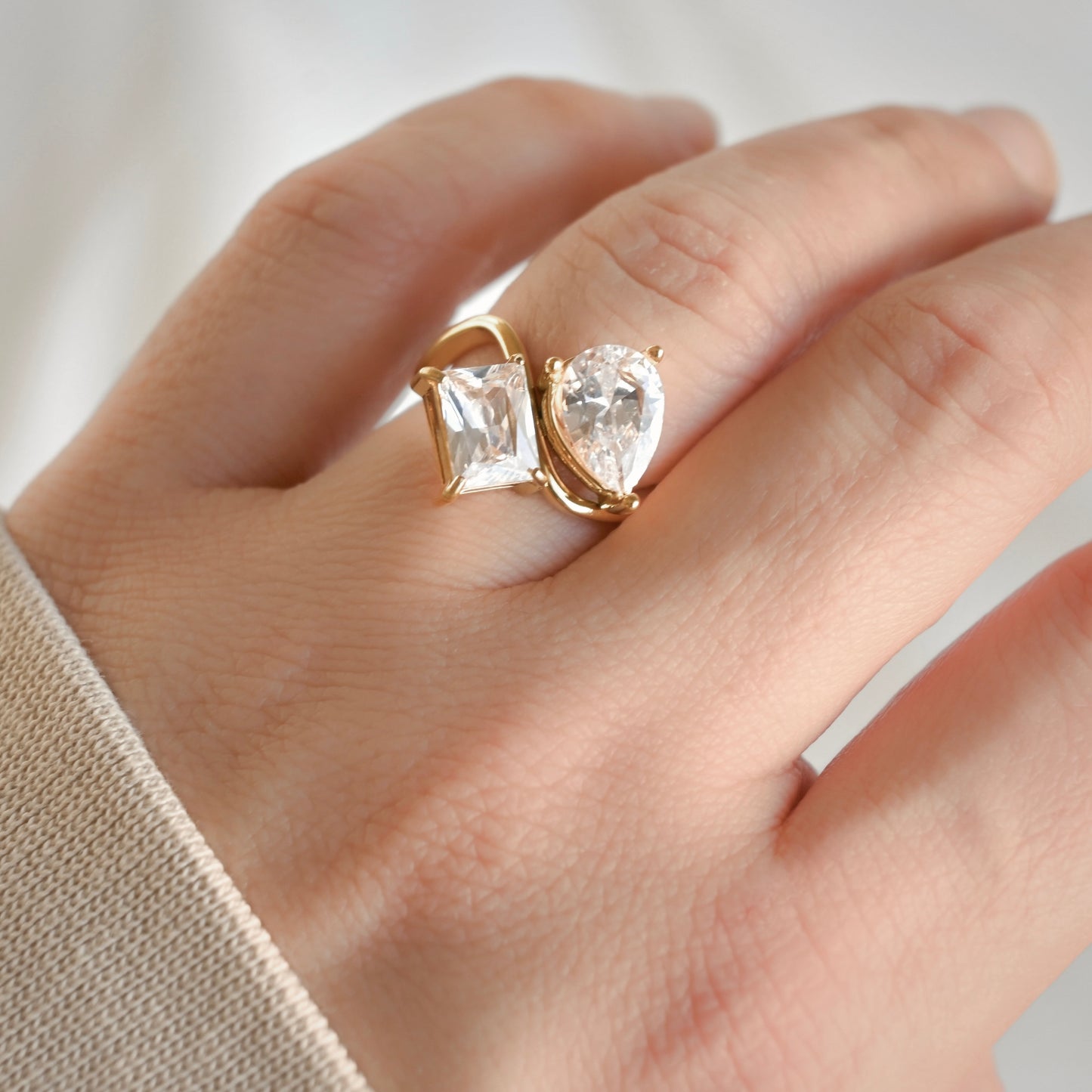 Hand wearing agold  toi et moi ring with white CZ on a neutral background