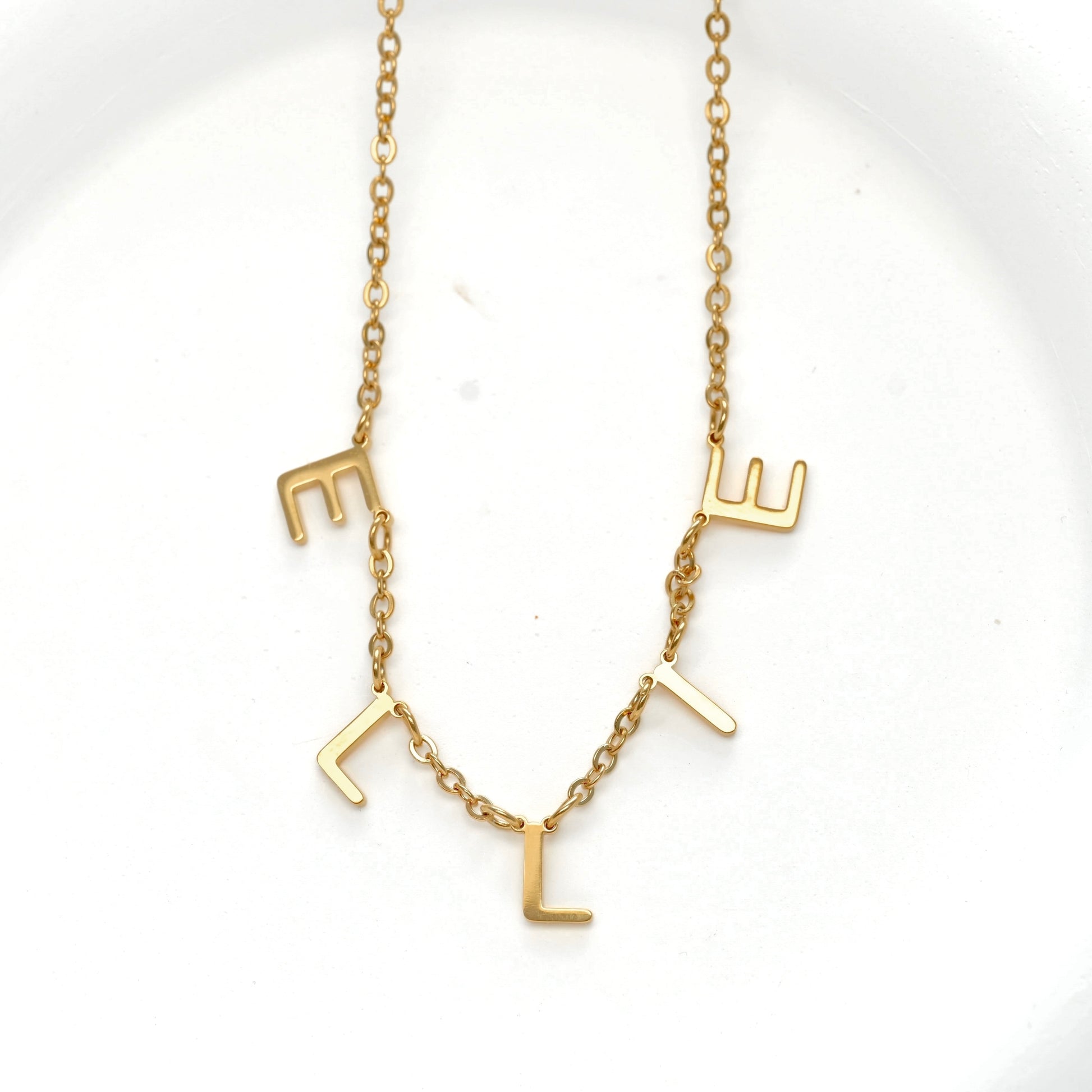 Front view of a gold initial necklace featuring the name 'ELLIE' spelled out with spaced individual letters, suspended from a delicate gold chain on a white background.