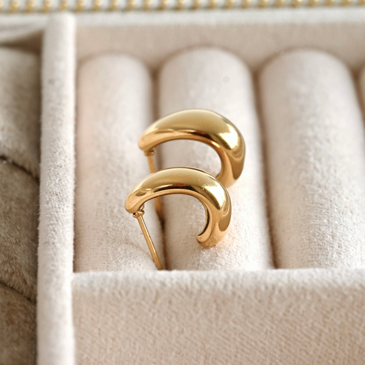 Pair of gold C hoop earrings on a soft beige cushion