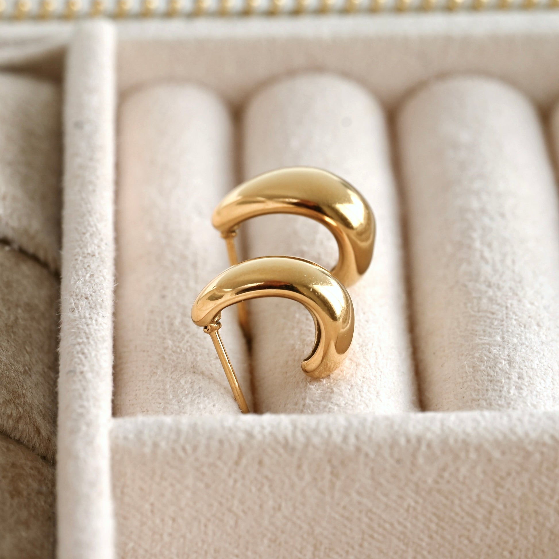 Pair of gold C hoop earrings on a soft beige cushion