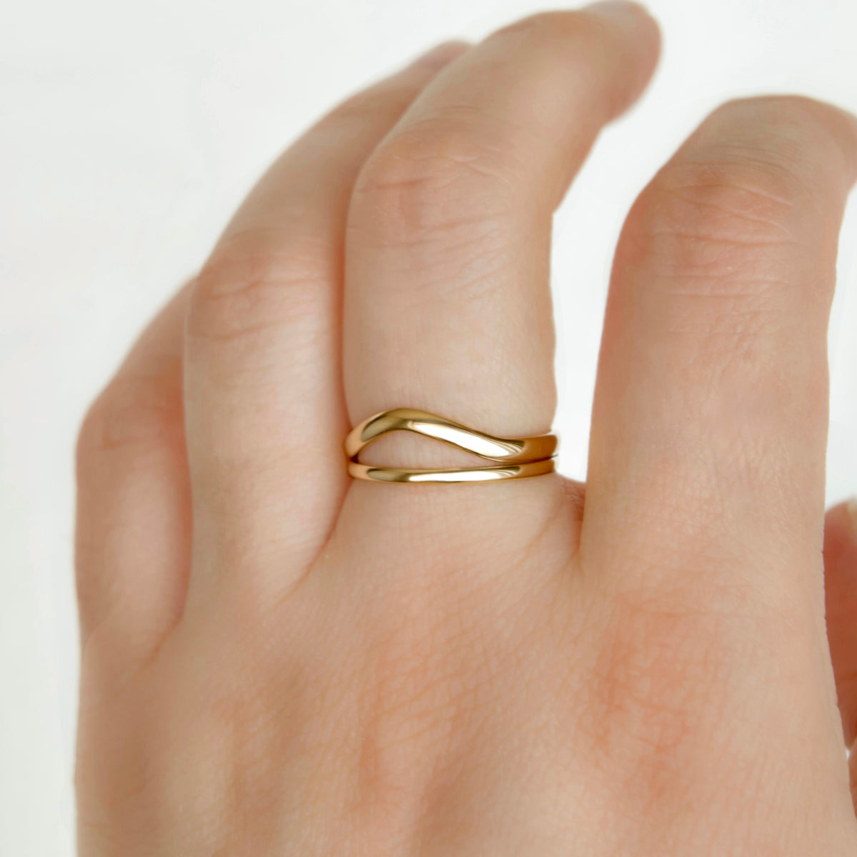 A close-up of a hand wearing a thin, polished gold ring with a wavy, intertwined double-band design.