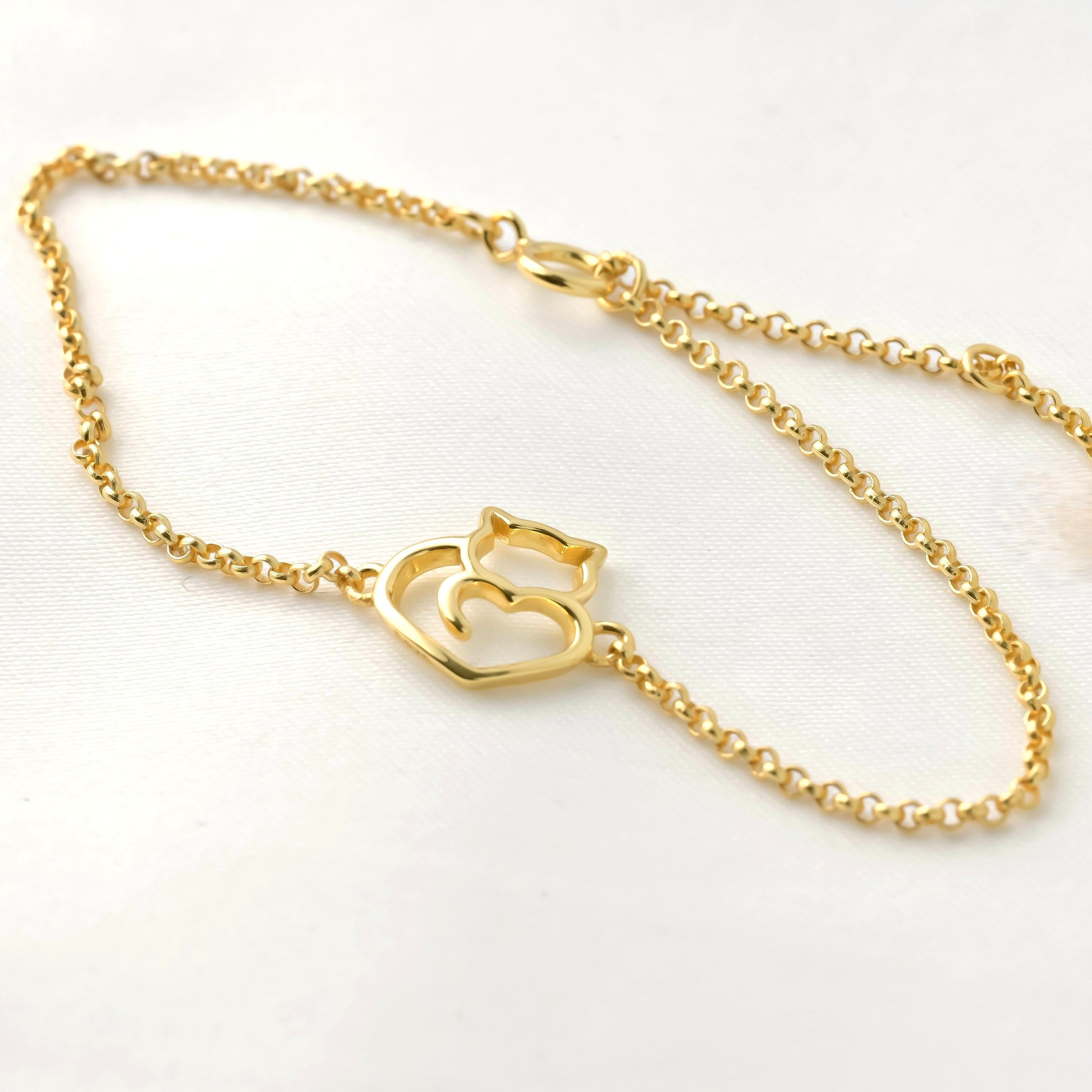 Close-up of dainty gold rolo bracelet with a heart-shaped cat charm on a white background