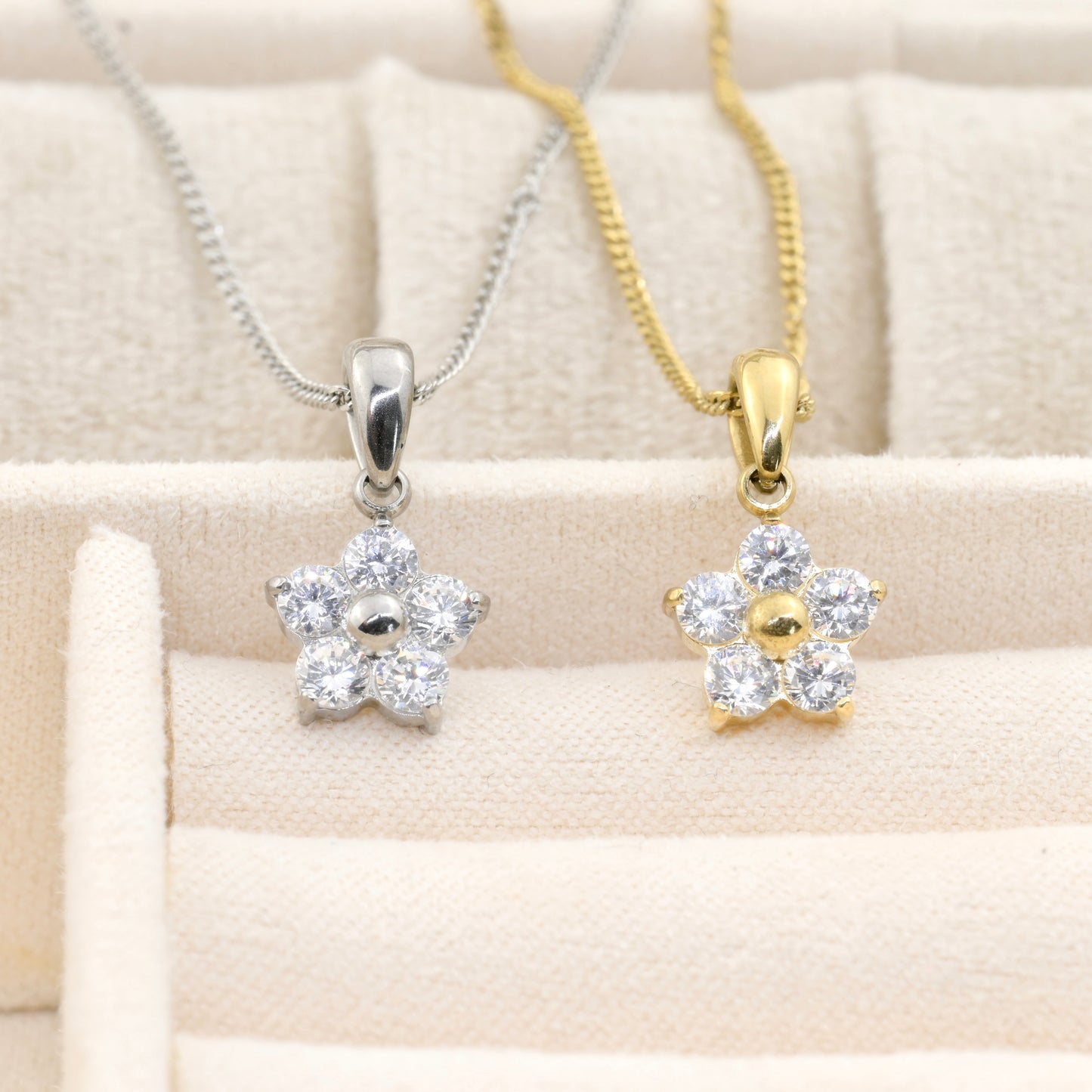 Two flower pendants, one silver and one gold, on a beige fabric background.