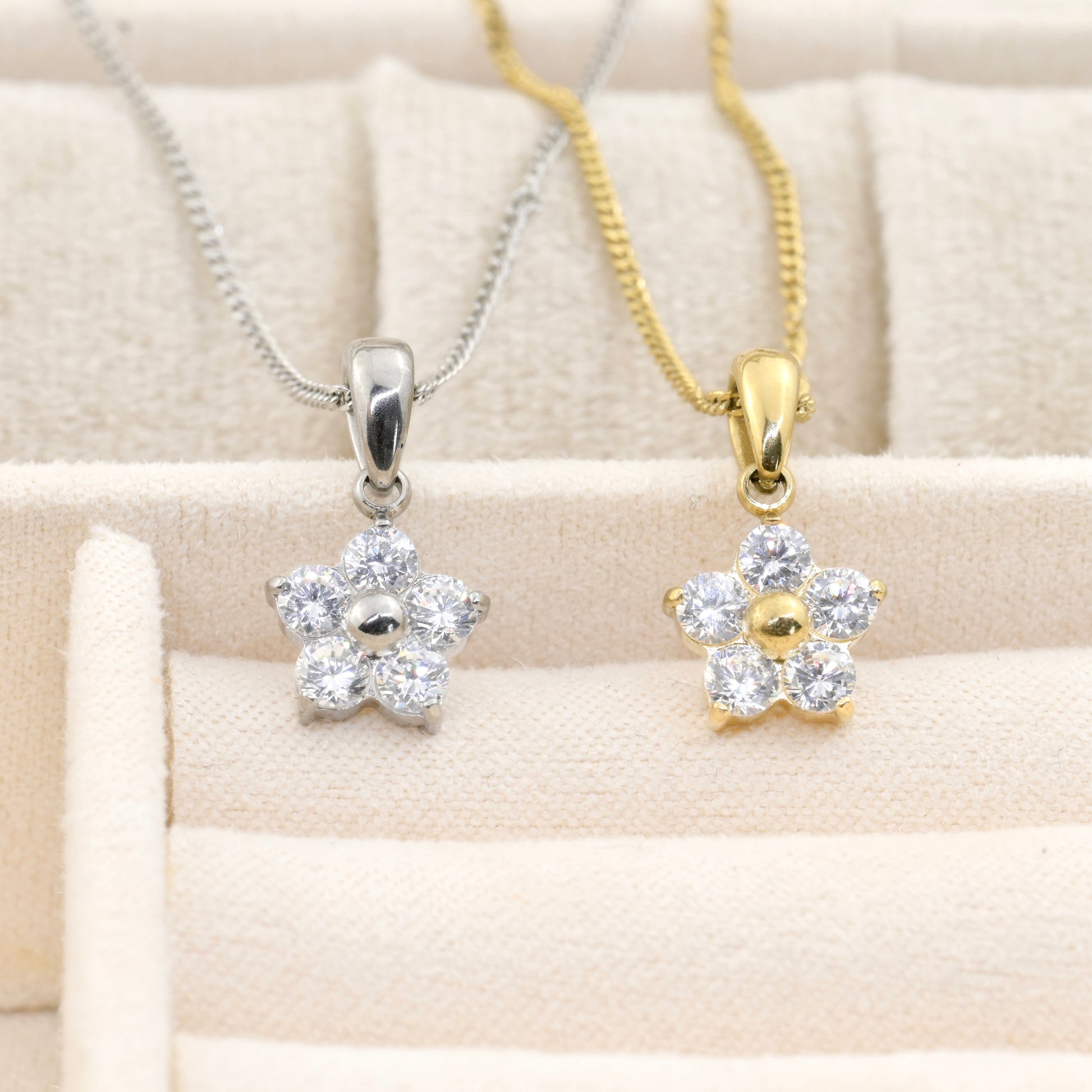 Two flower pendants, one silver and one gold, on a beige fabric background.