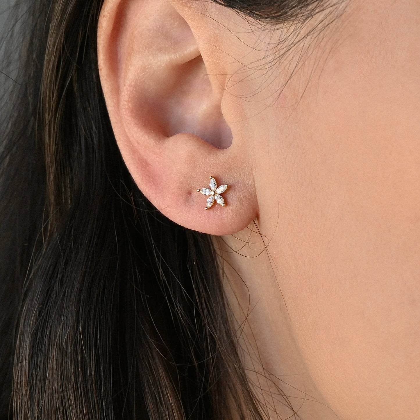 Close-up of an ear wearing a silver flower stud earring with CZ stones
