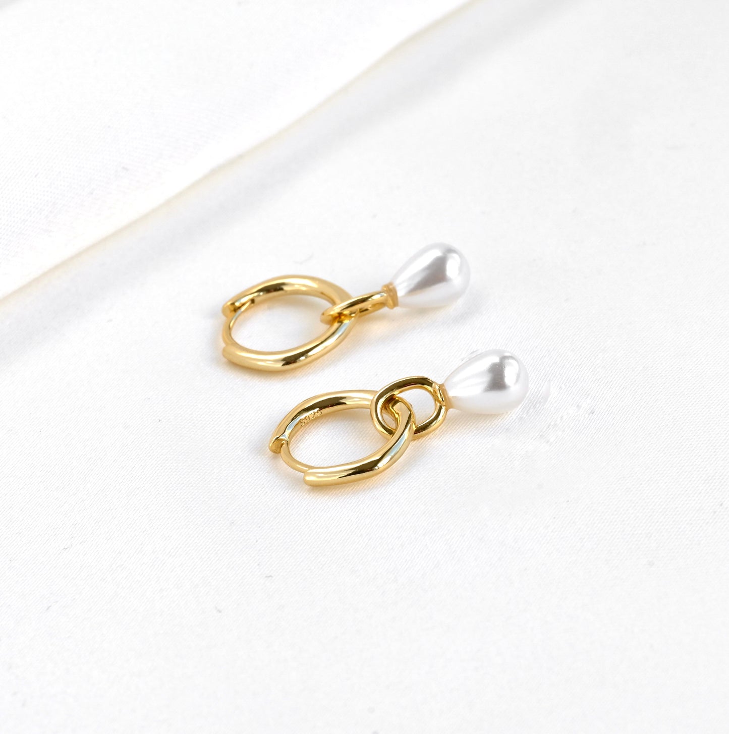 Sterling silver gold earrings with synthetic teardrop pearl charms on a white background