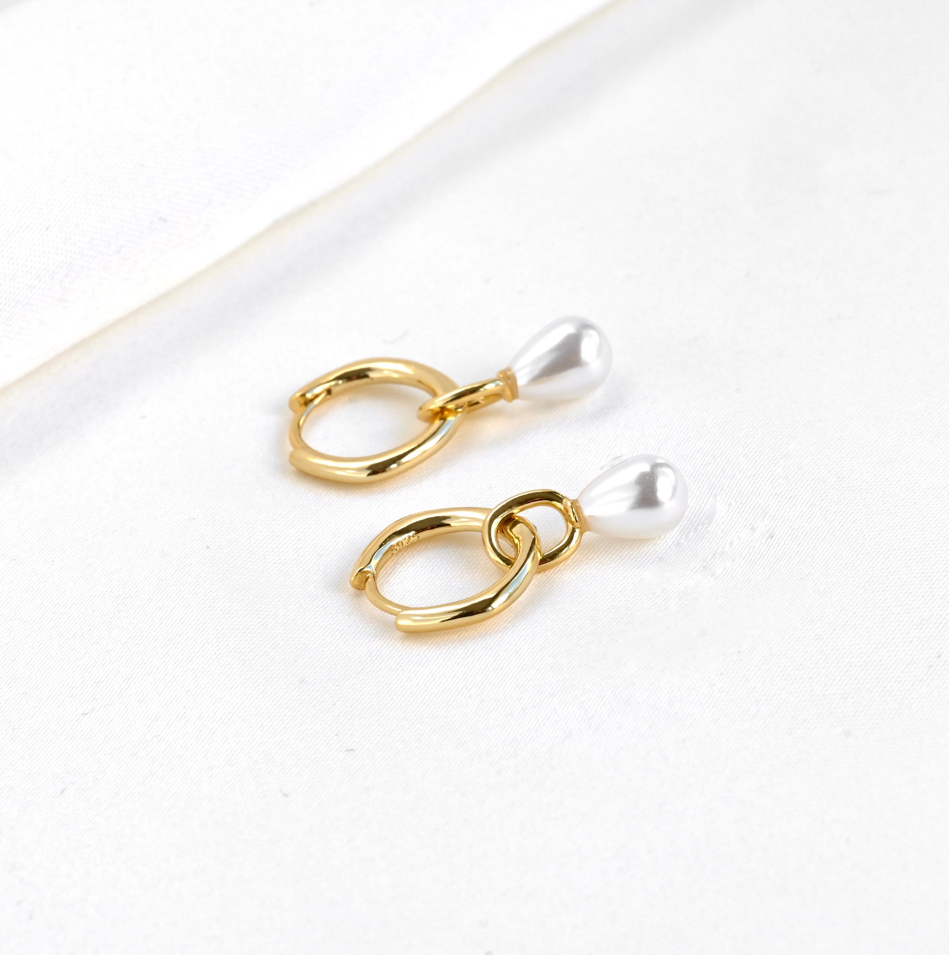 Sterling silver gold earrings with synthetic teardrop pearl charms on a white background