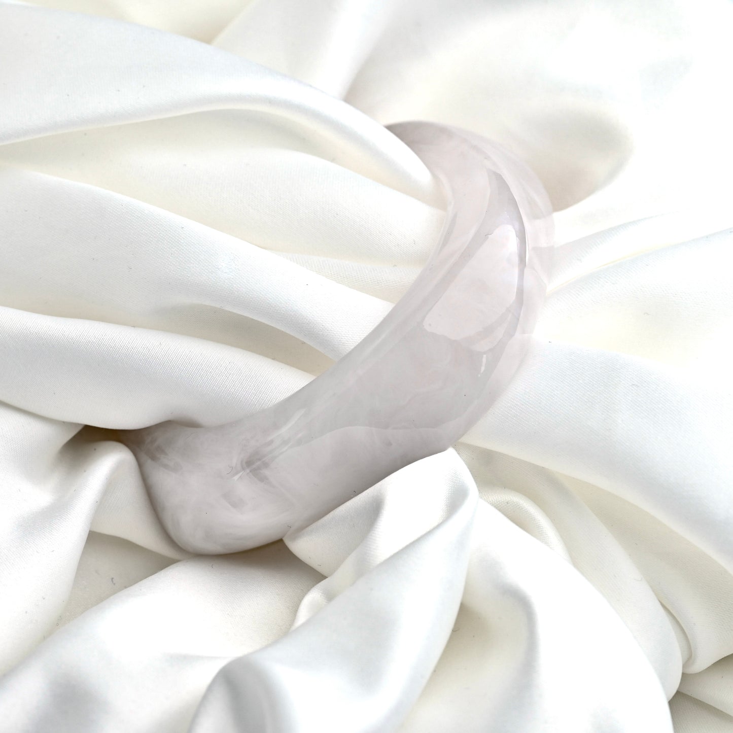 A chunky translucent pale gray resinbangle resting on draped white satin fabric.