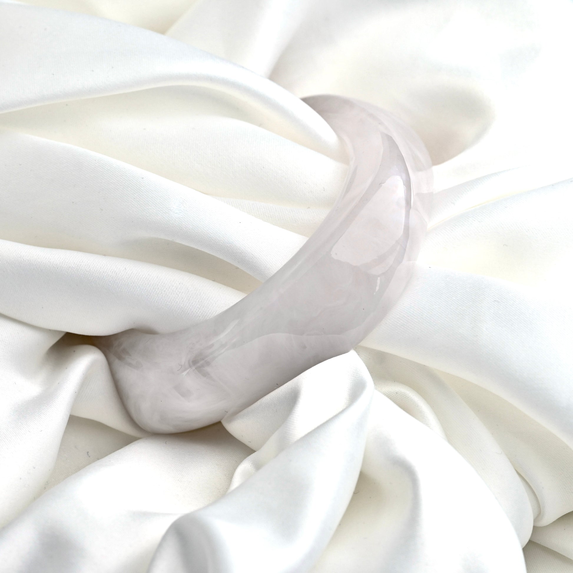 A chunky translucent pale gray resinbangle resting on draped white satin fabric.