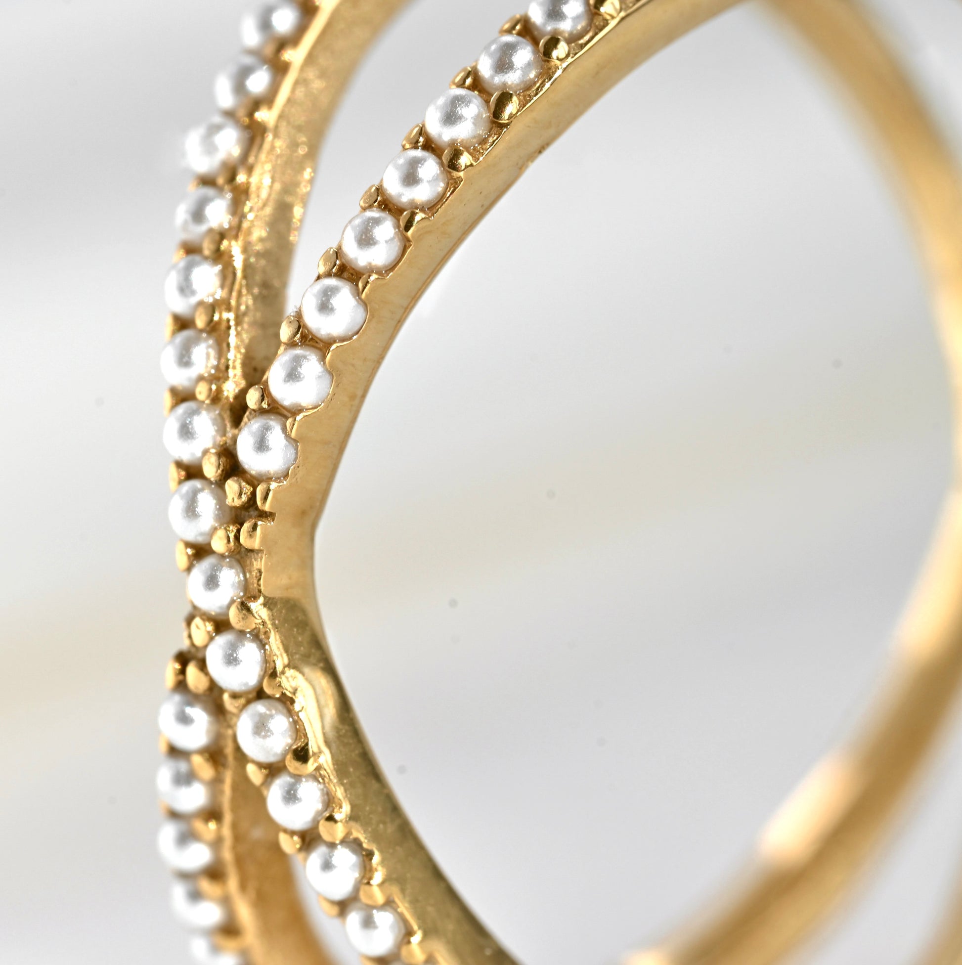 Close-up of gold X ring with small pearls ina pave setting on a light background
