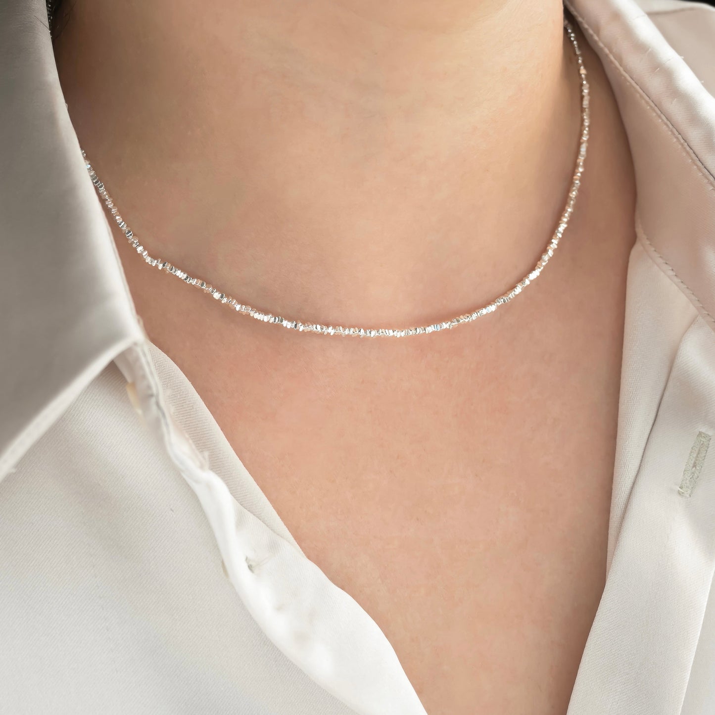 Silver necklace with tiny sterling silver square beads on a person wearing a white shirt