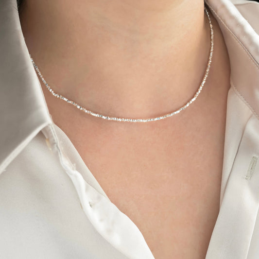 Silver necklace with tiny sterling silver square beads on a person wearing a white shirt