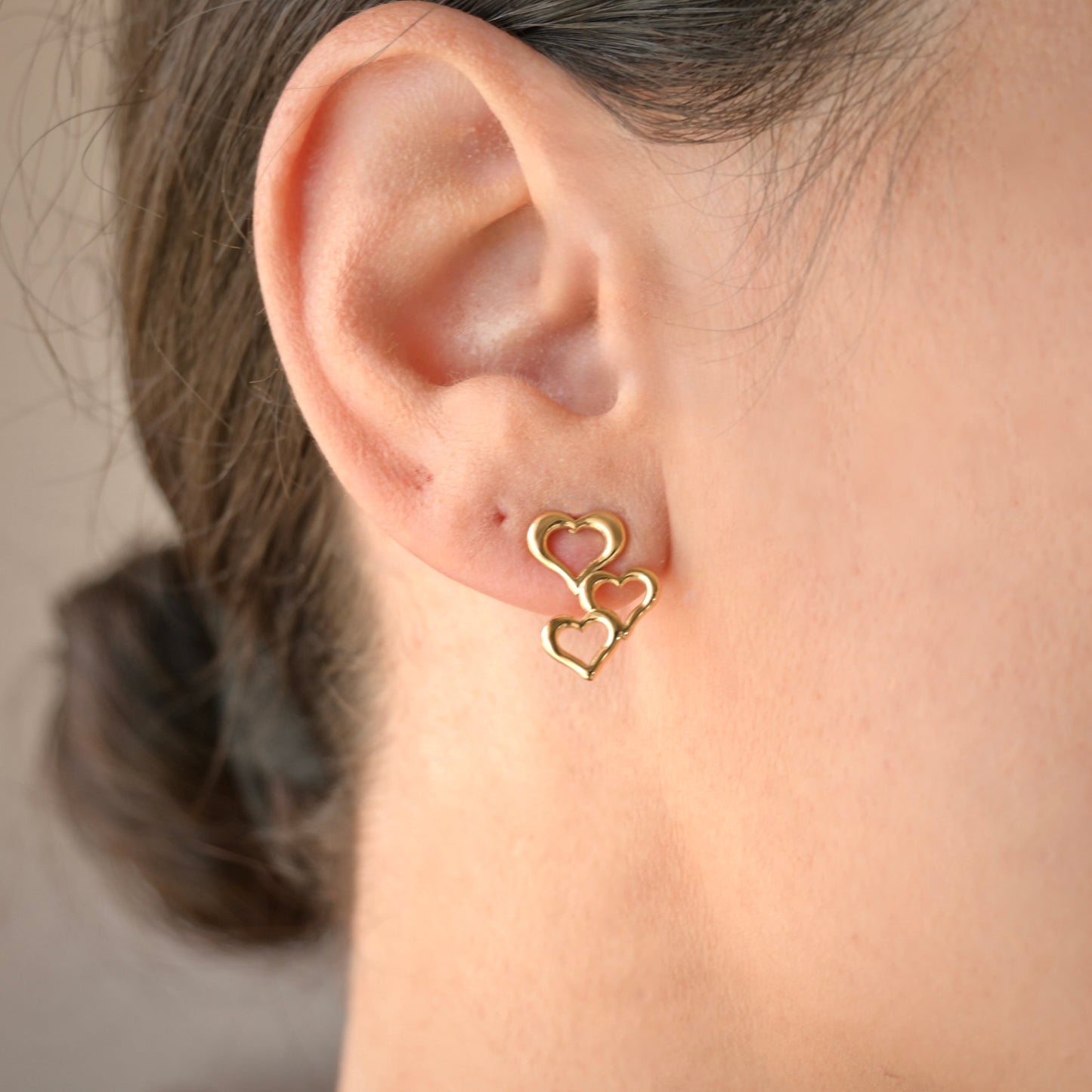 Gold heart-shaped earrings worn by a person with a neutral background