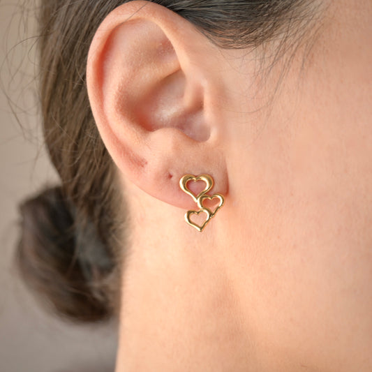 Gold heart-shaped earrings worn by a person with a neutral background