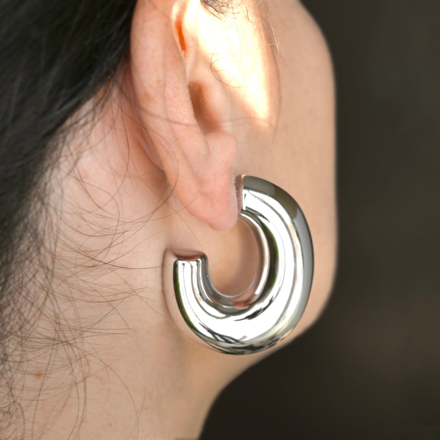 Ultra thick silver hoop earring worn on an ear with a dark background