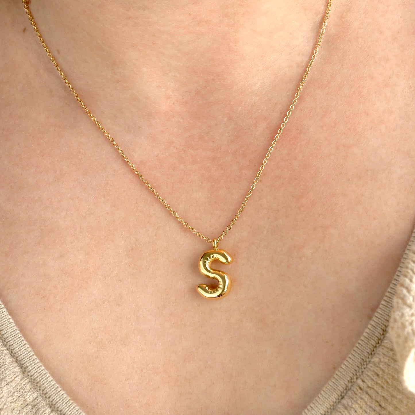 Gold initial necklace with an 'S' pendant on a person's neck