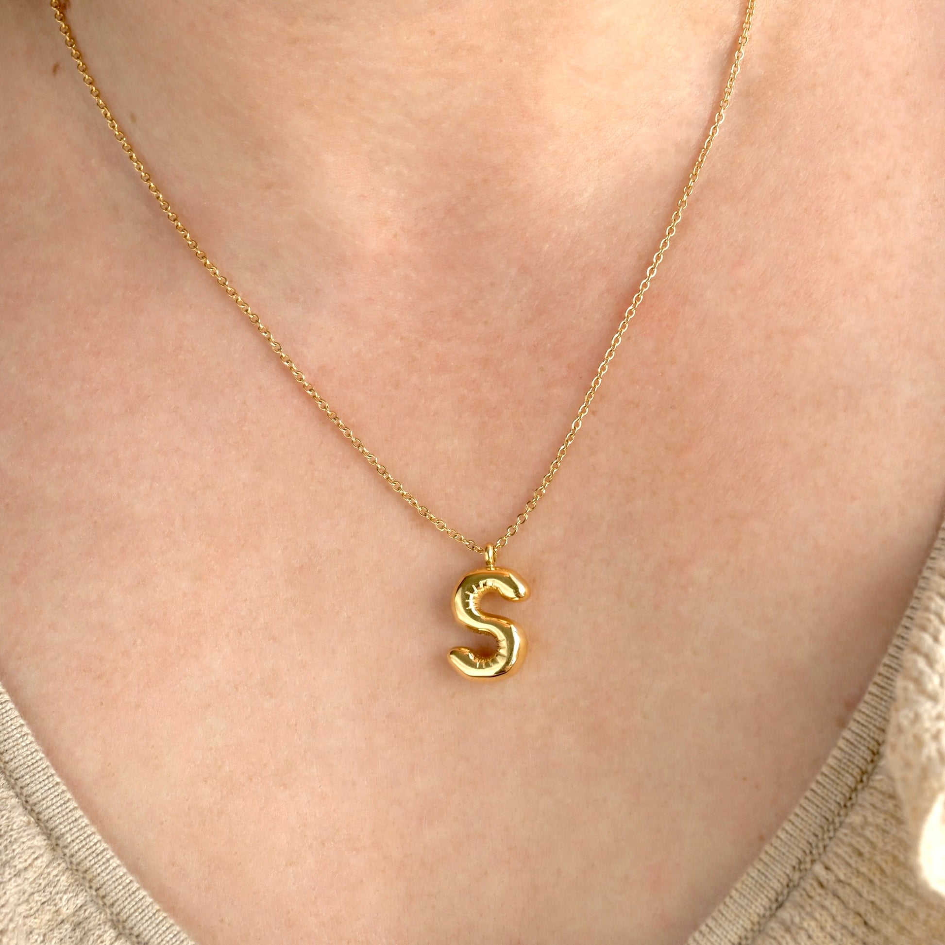 Gold initial necklace with an 'S' pendant on a person's neck