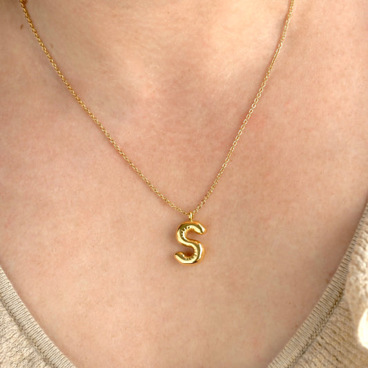 Gold initial necklace with an 'S' pendant on a person's neck