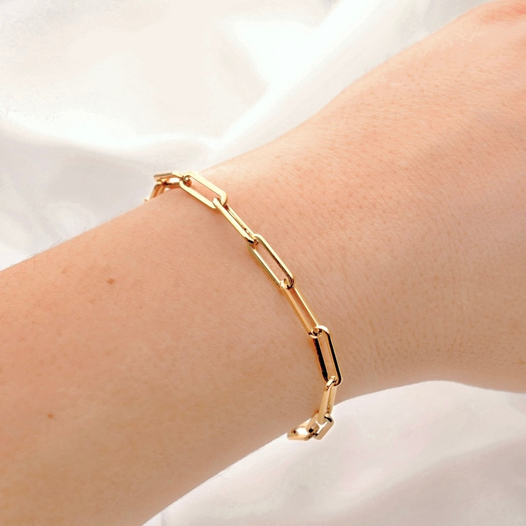 Gold paperclip chain bracelet on a wrist against a white background