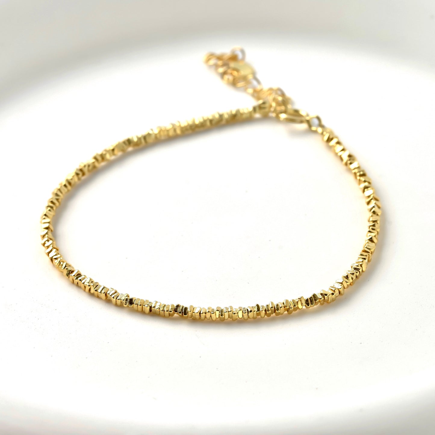 Gold bracelet with stering silver square beadson a white background