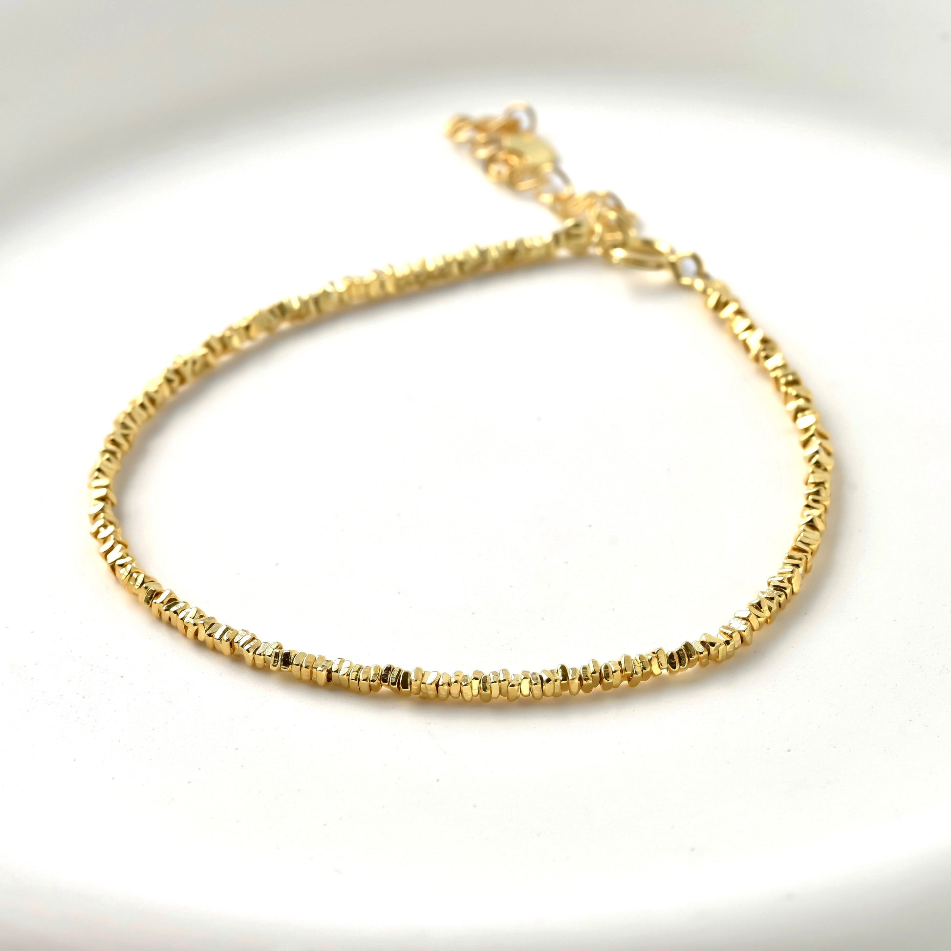 Gold bracelet with stering silver square beadson a white background