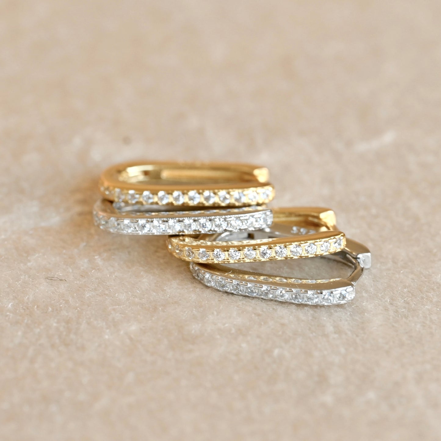 Two pairs of gold and silver clicker hoops stacked on a beige surface