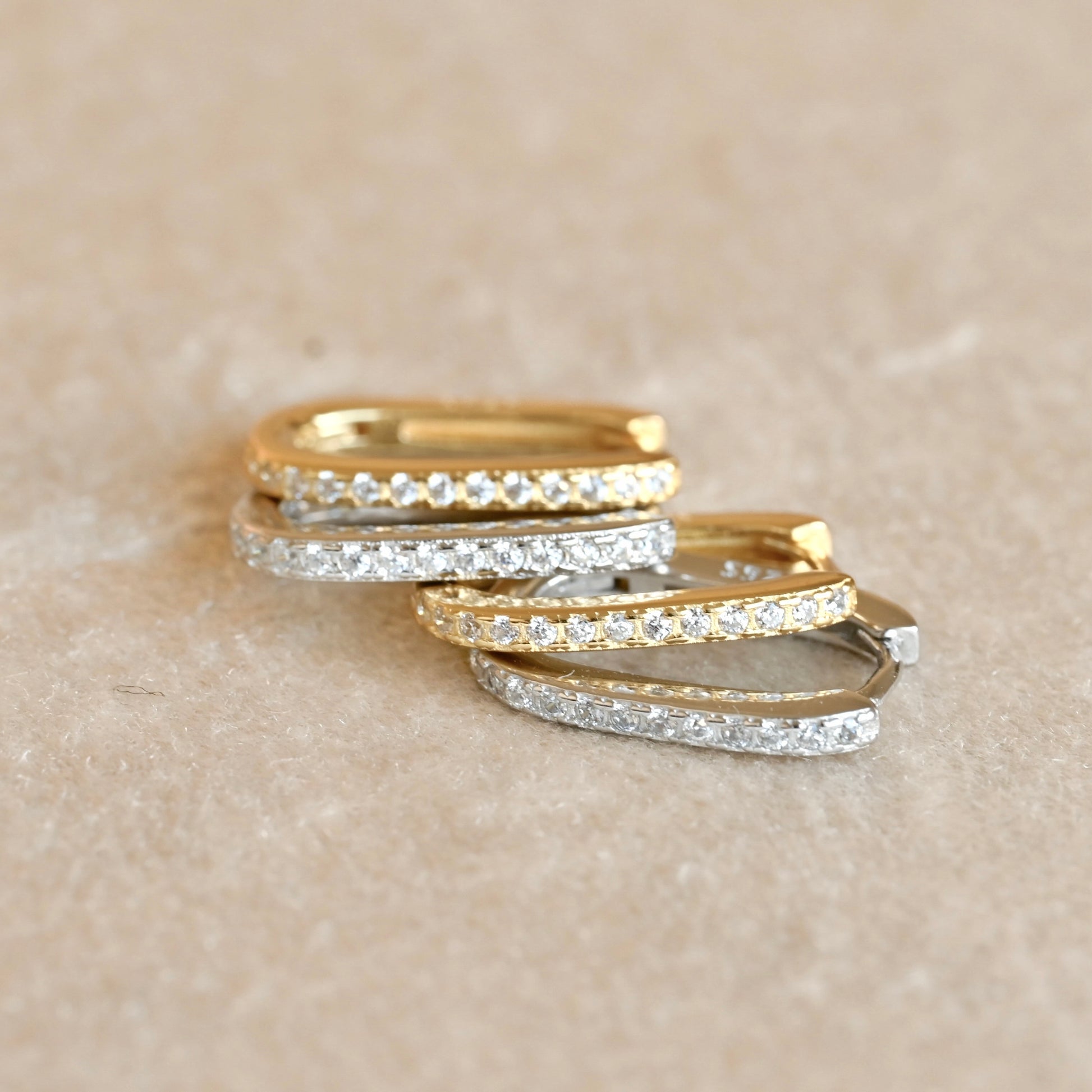 Two pairs of gold and silver clicker hoops stacked on a beige surface