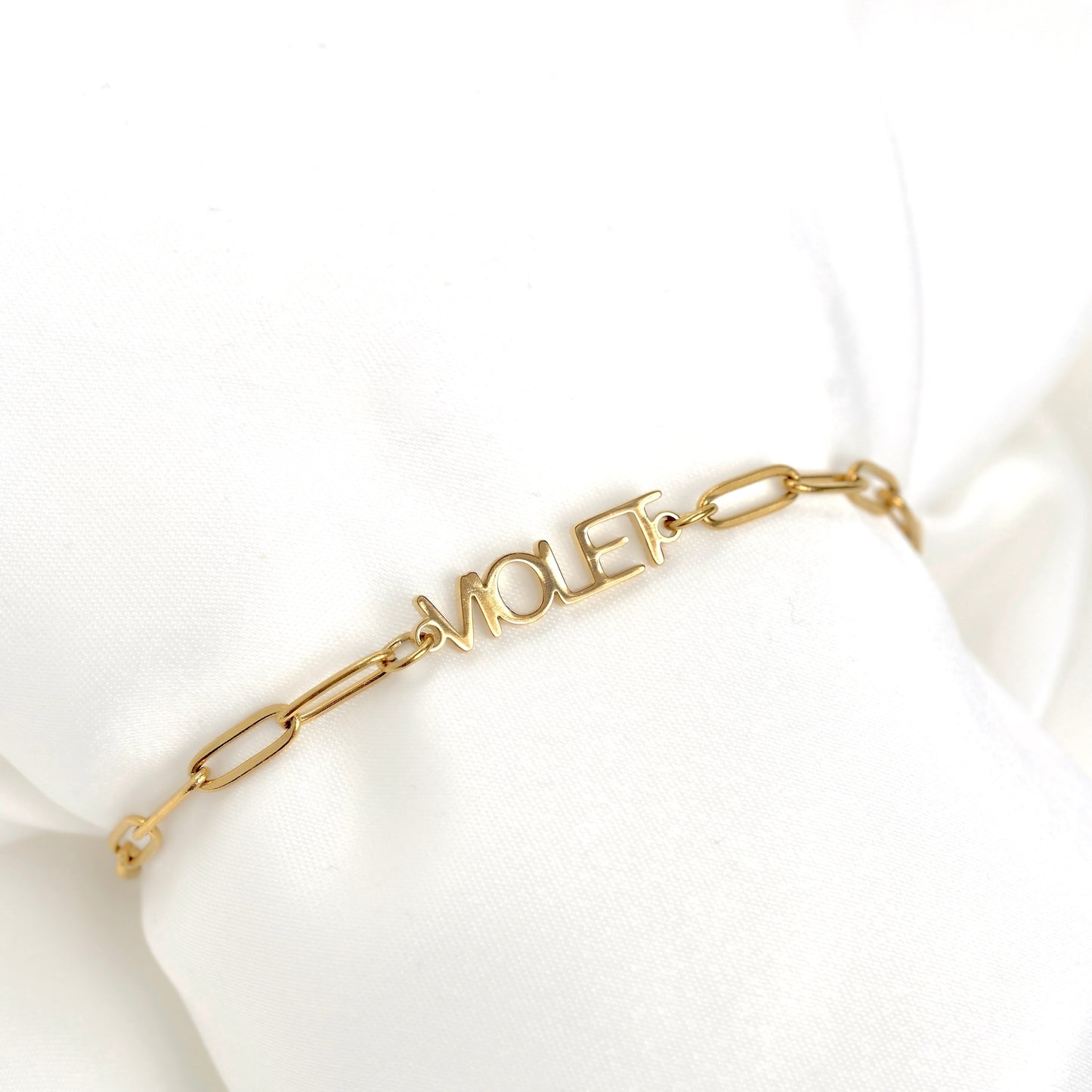 A gold chain bracelet with a central 'VIOLET' nameplate, displayed on a white fabric wrist form.