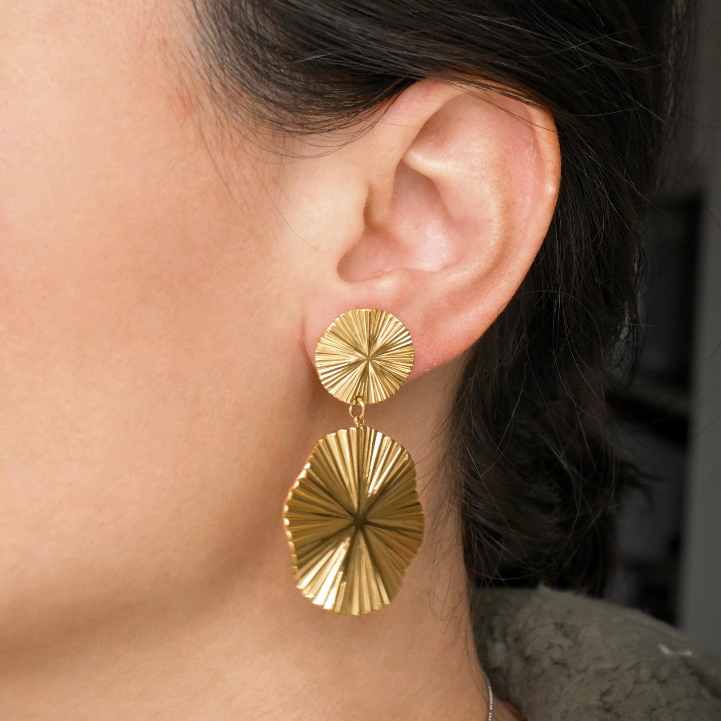 Gold earrings worn by a person with dark hair.