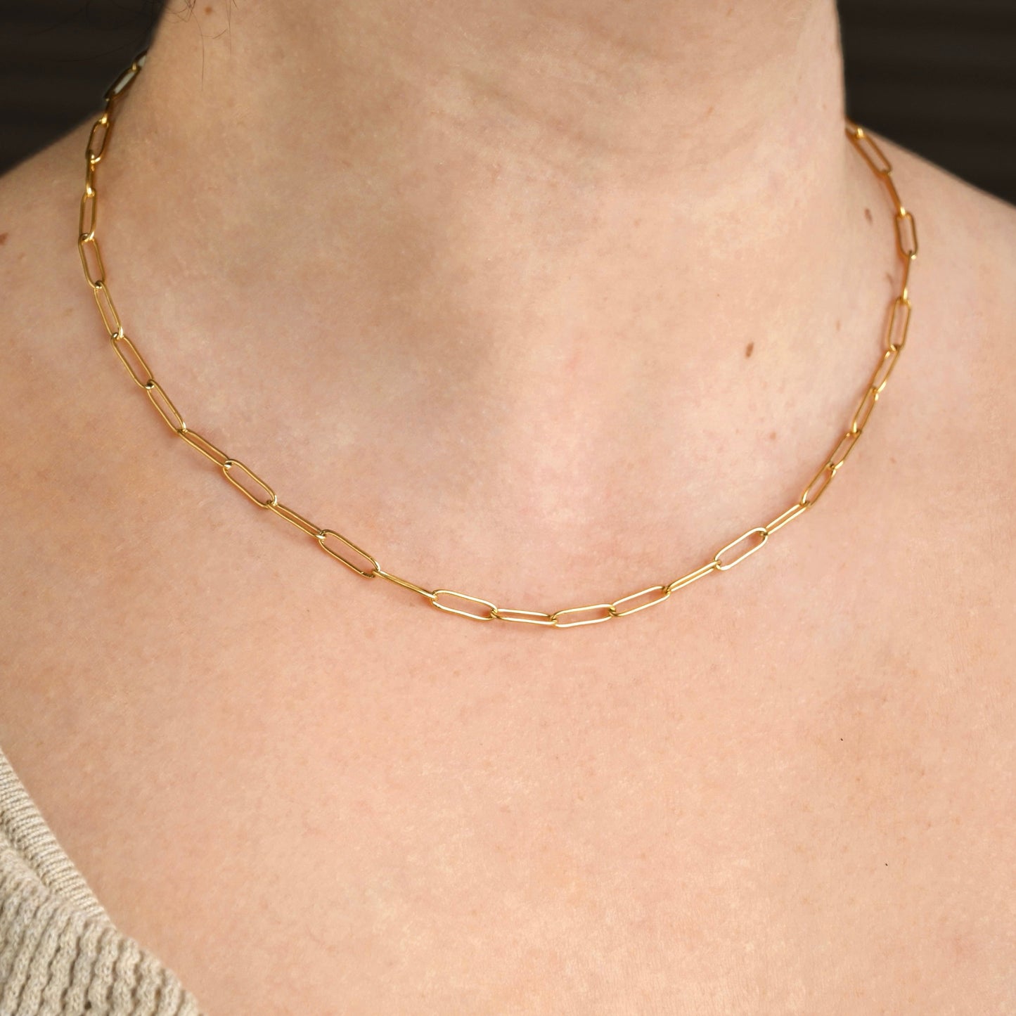 Gold paperclip chain necklace worn by a person with a neutral background