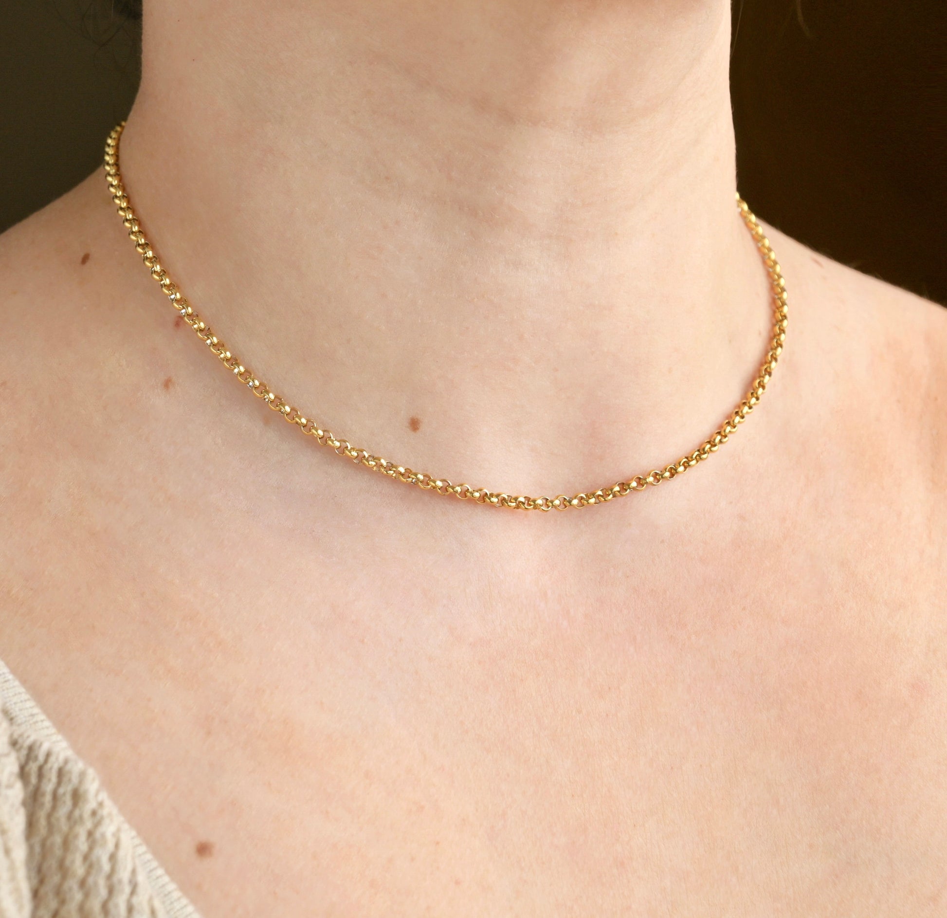 3mm gold rolo necklace on a person's neck with a neutral background