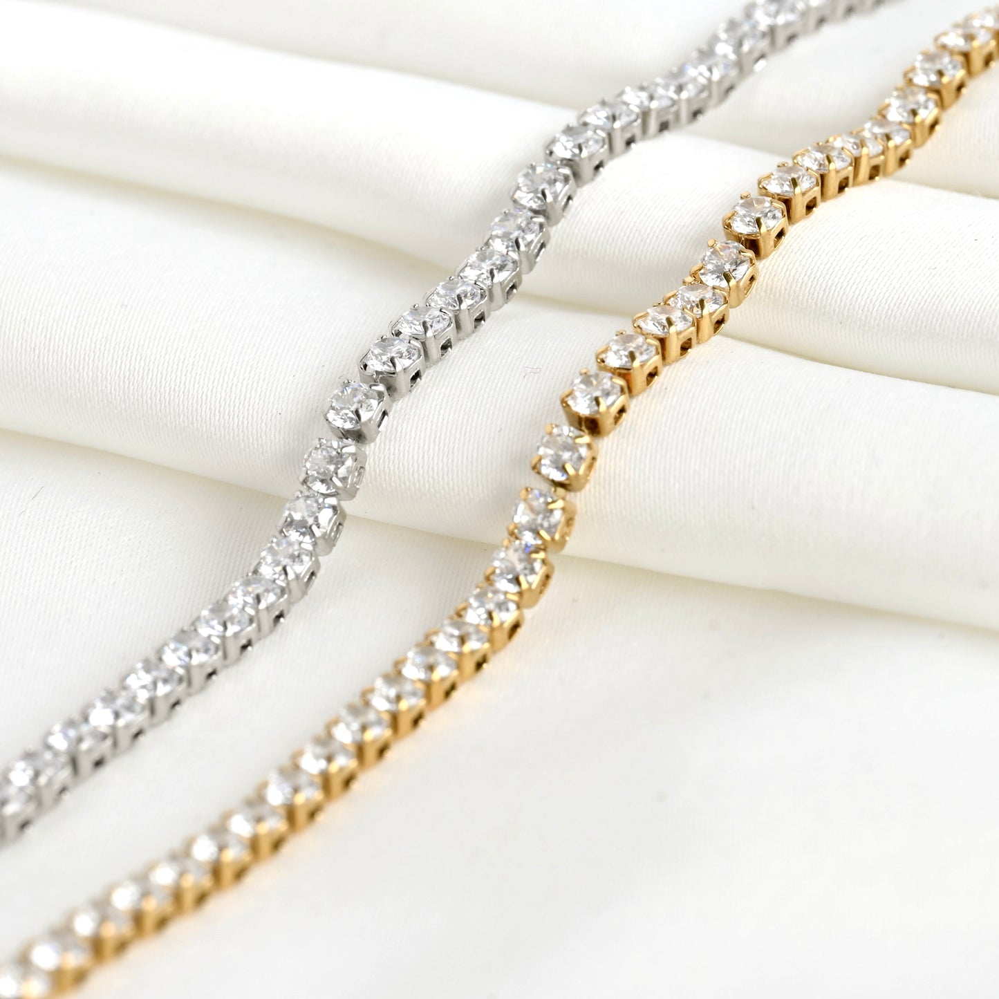 Two diamond bracelets, one silver and one gold, on a white fabric background.