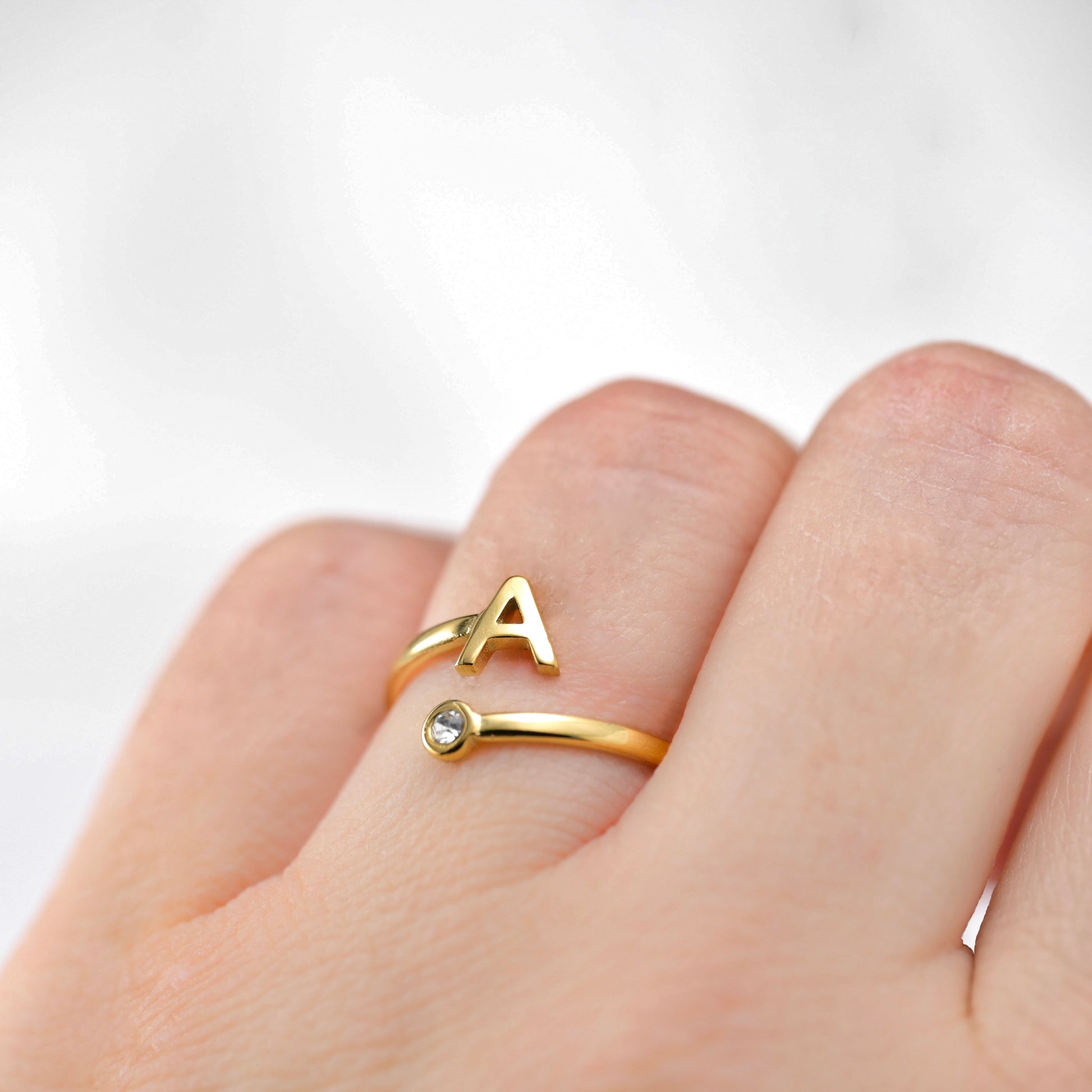 Open Gold ring with letter 'A' on a finger against a white background