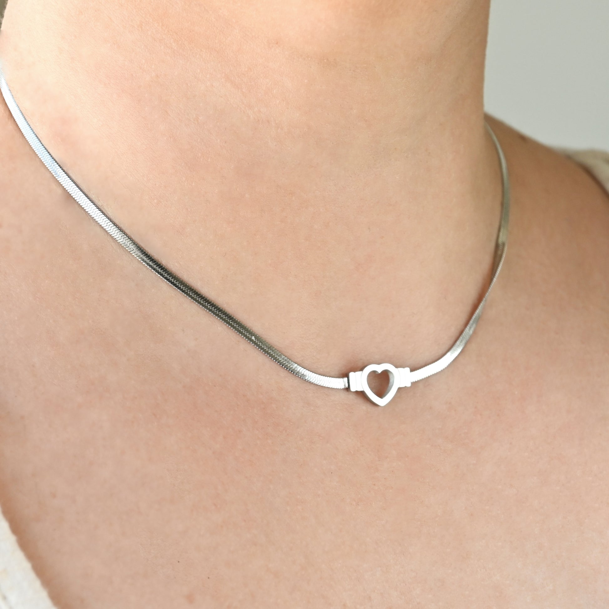 Silver herringbone heart necklace on a person's neck against a neutral background