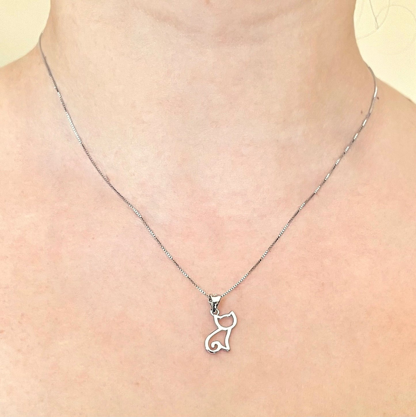 Front view of silver cat pendant necklace on a person's neck against a neutral background