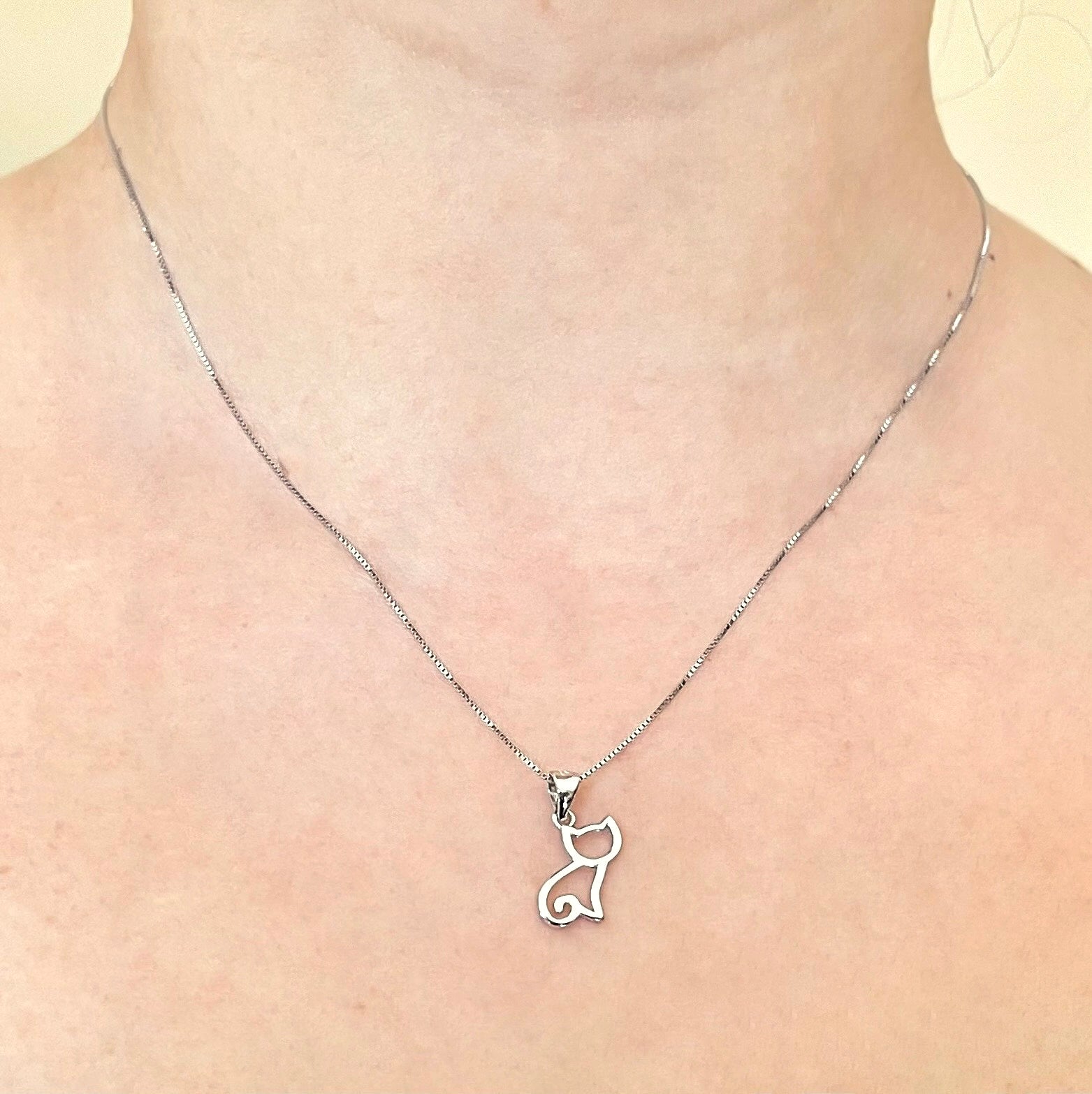 Front view of silver cat pendant necklace on a person's neck against a neutral background