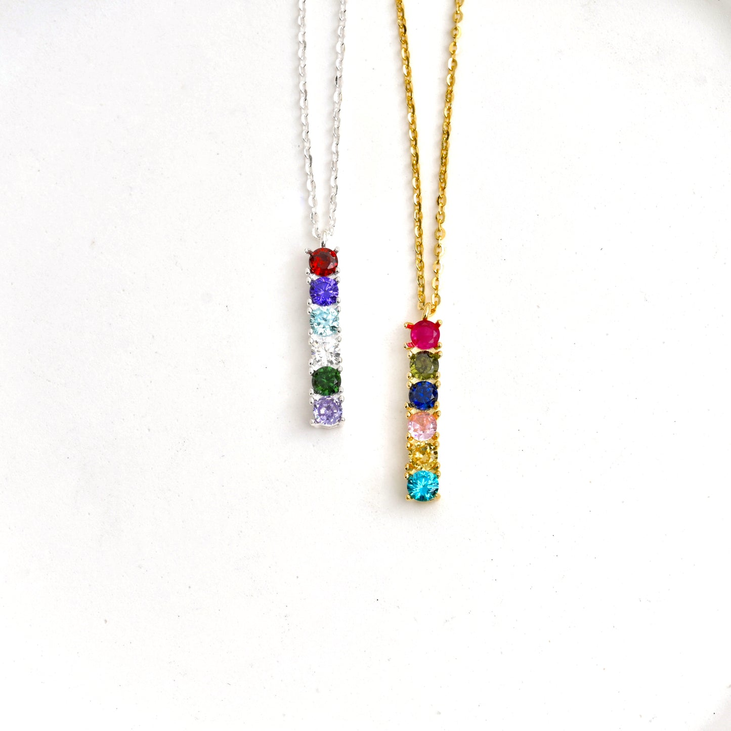 Two personalized birthstone bar necklaces, one gold and one silver, with colorful CZ stones on a white background