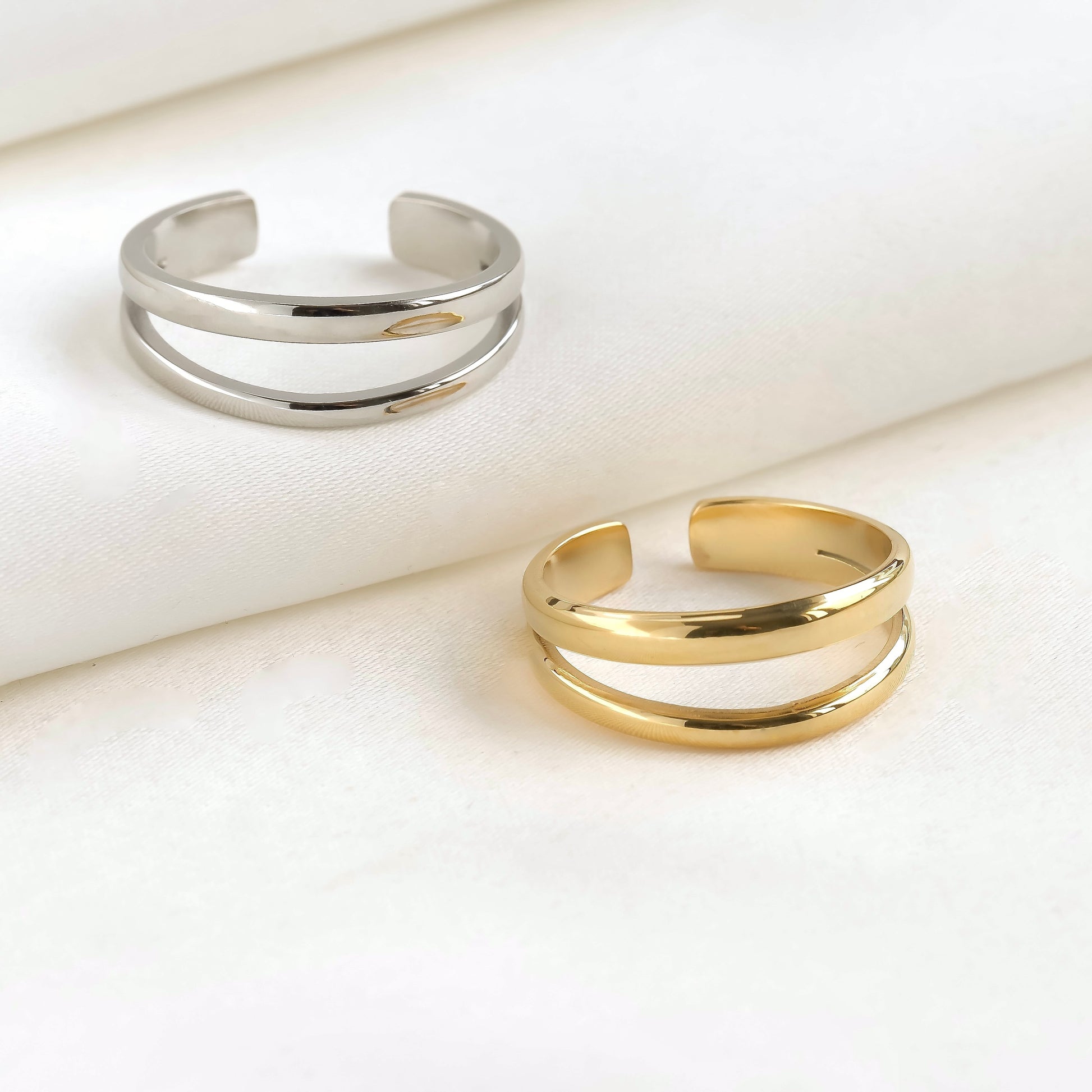 Two gold and silver open rings on a light beige surface