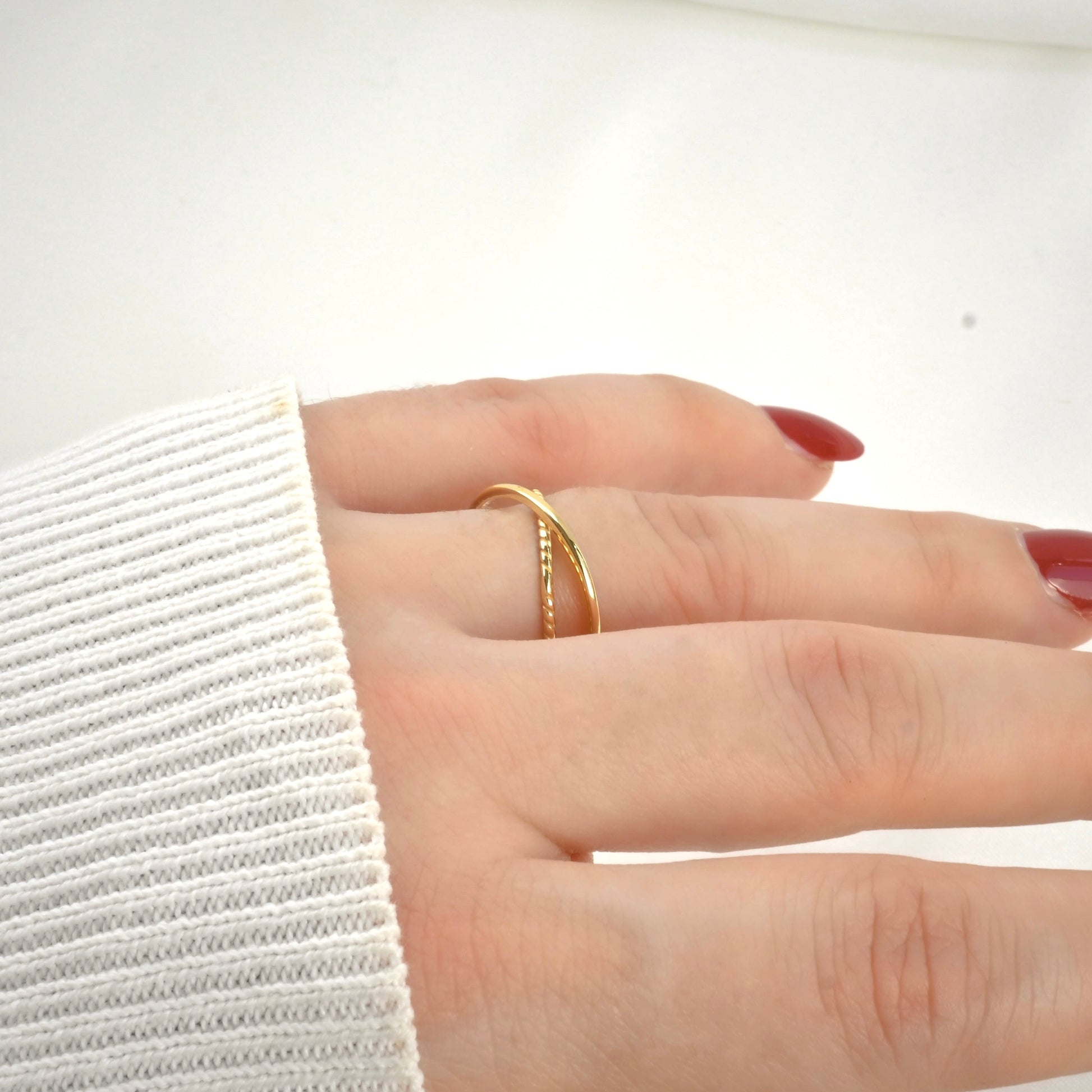Side view of Hand wearing a criss cross  gold ring on a white background