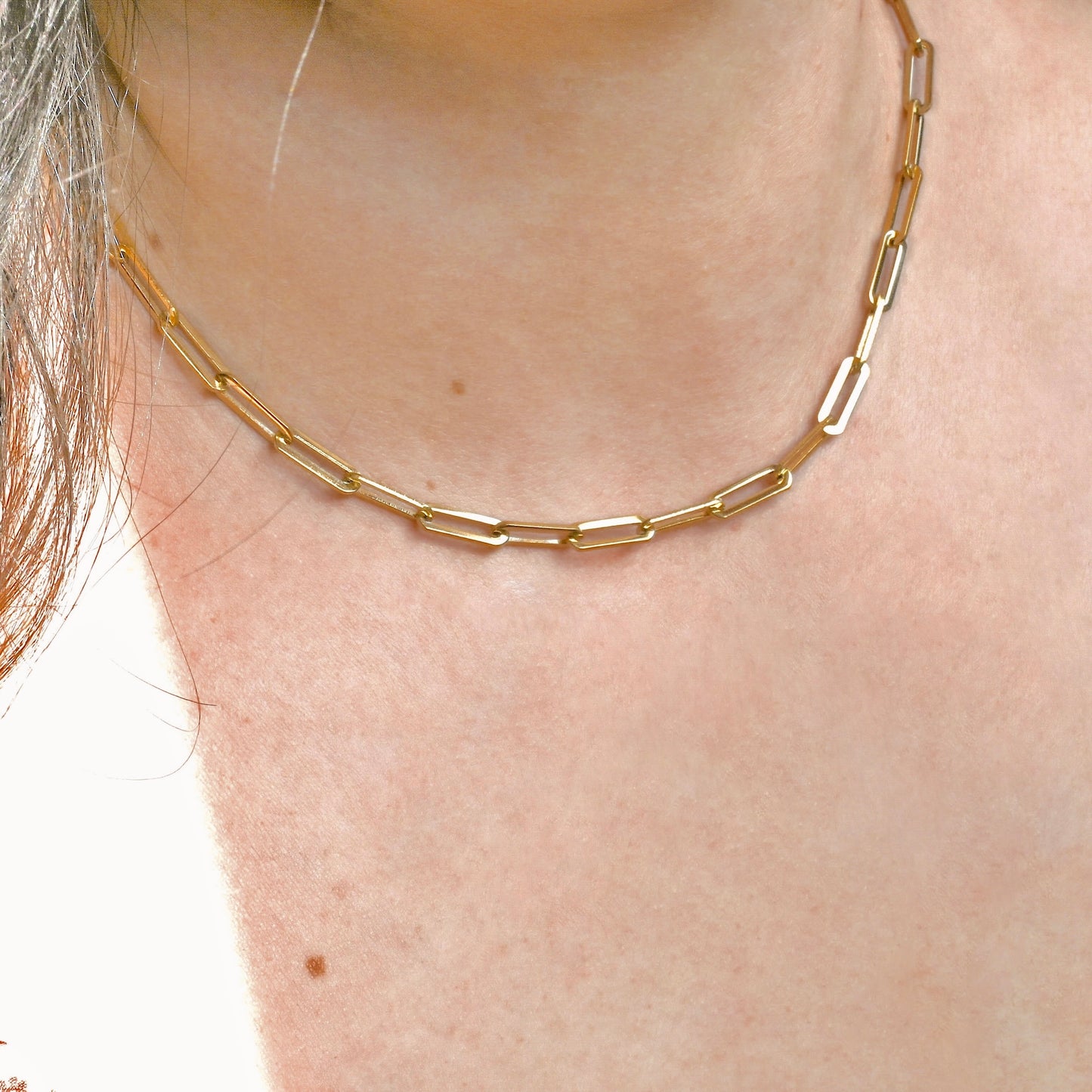 Gold paperclip necklace on a person's neck with a plain background