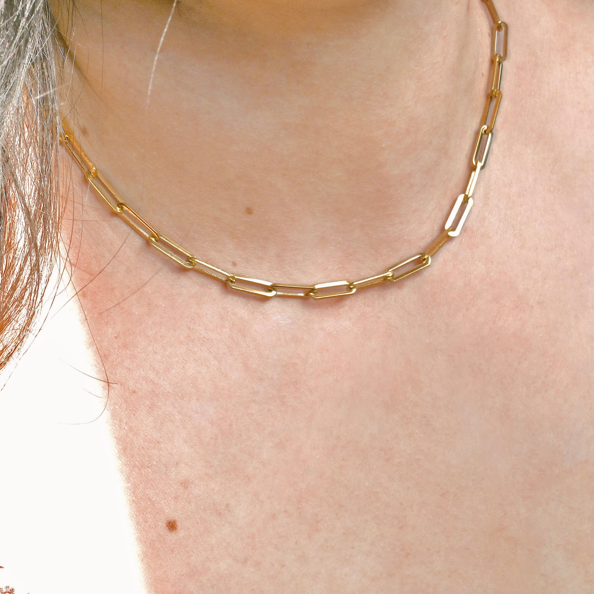 Gold paperclip necklace on a person's neck with a plain background