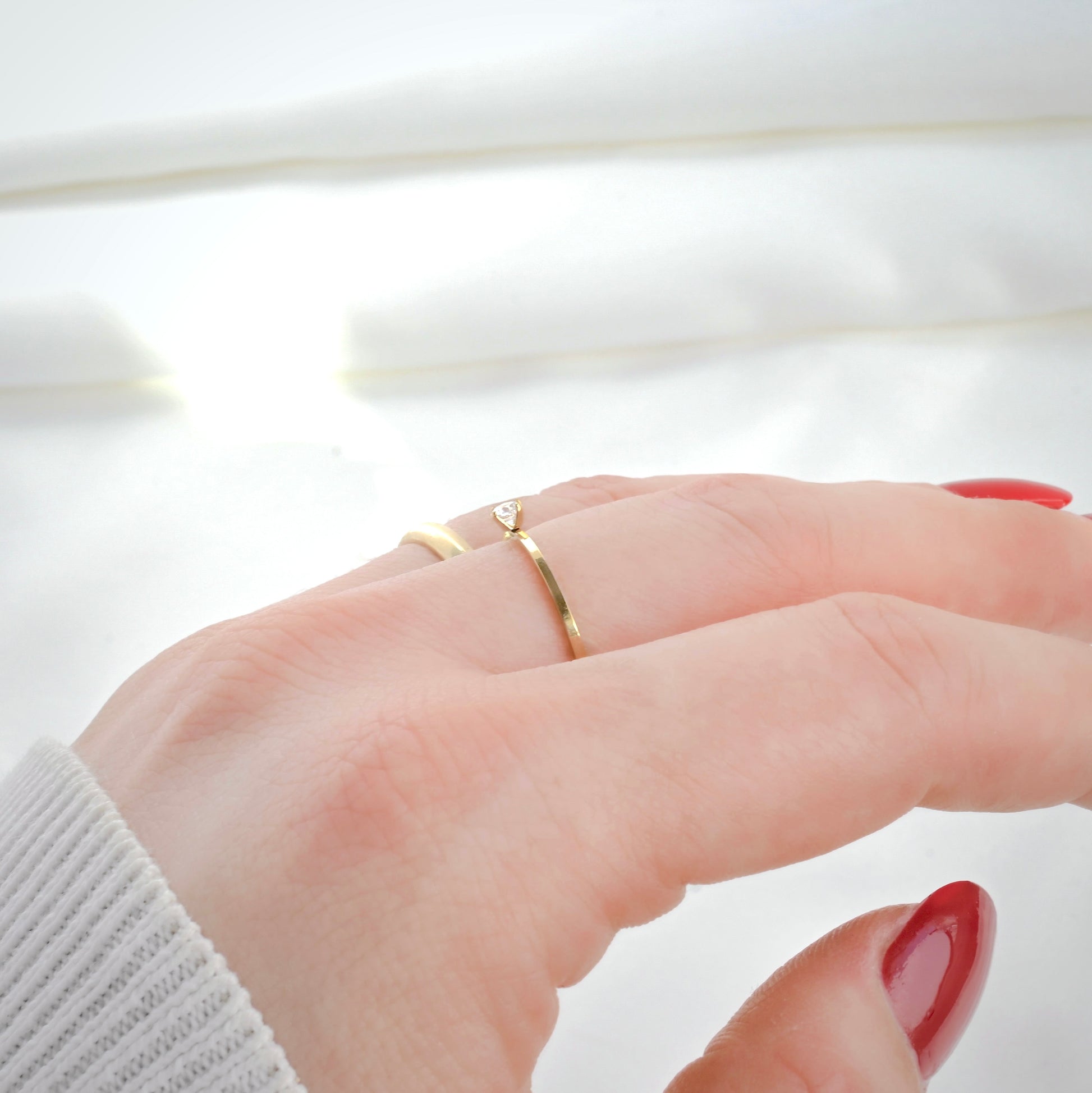 Close-up side view of a hand wearing two gold rings on a light background
