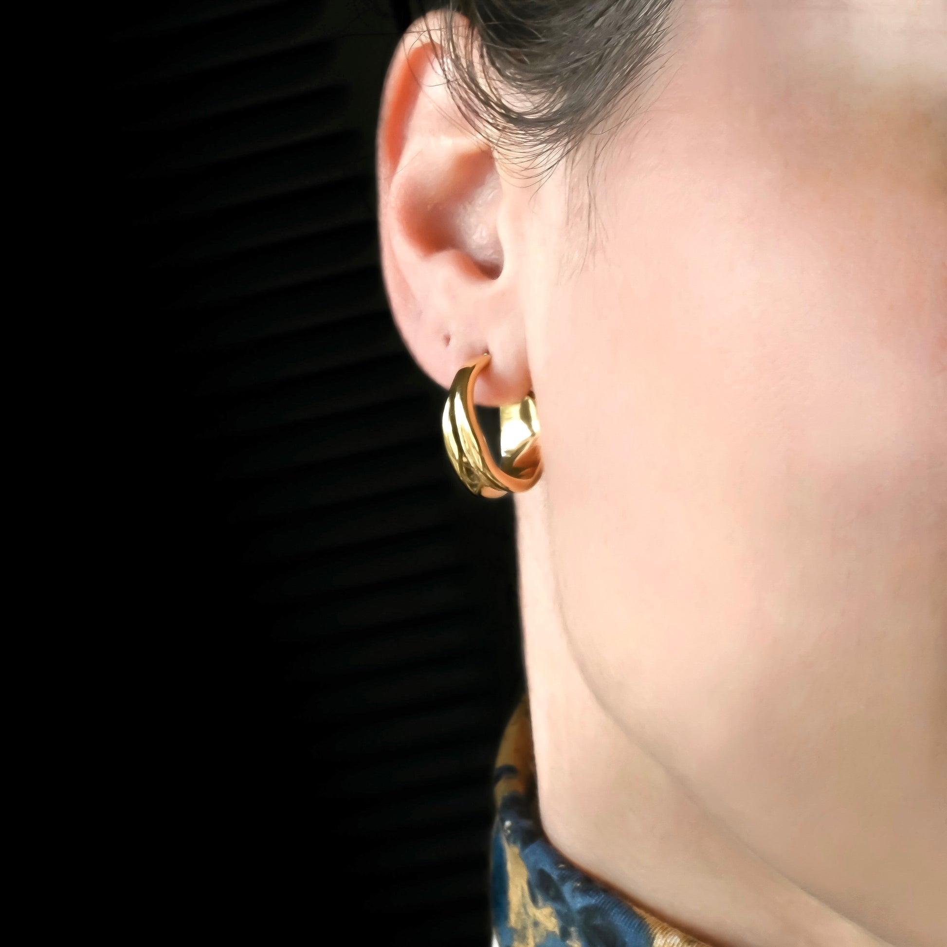 Chunky gold hoop earring worn by a person against a dark background