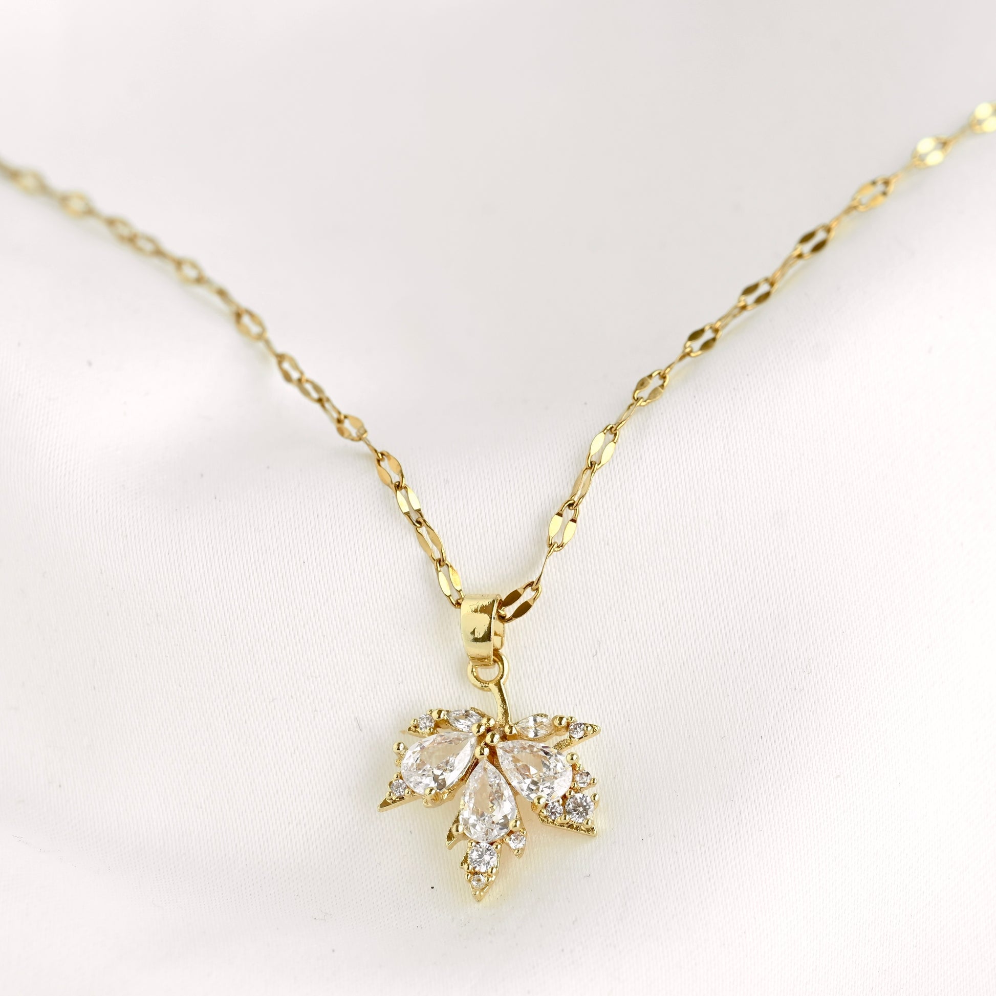 A gold chain necklace with a small leaf-shaped pendant set with clear stones, displayed on a soft white background.