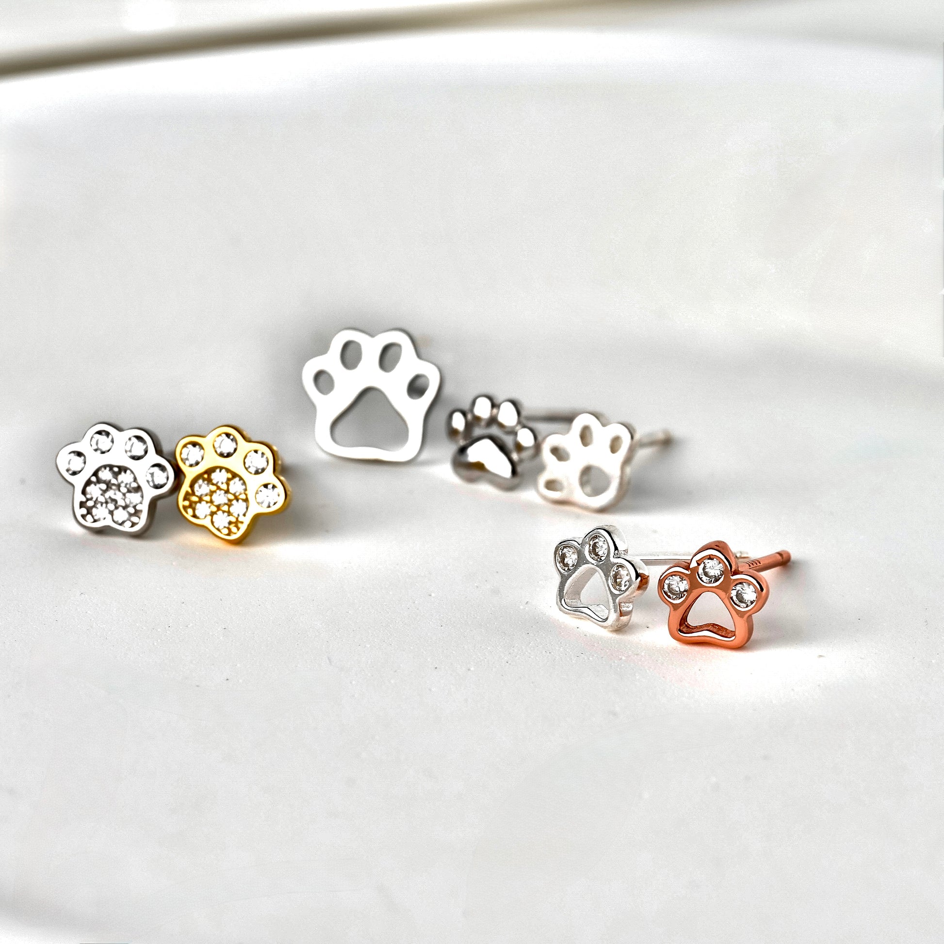 Set of paw-shaped earrings in silver, gold, and rose gold on a white background