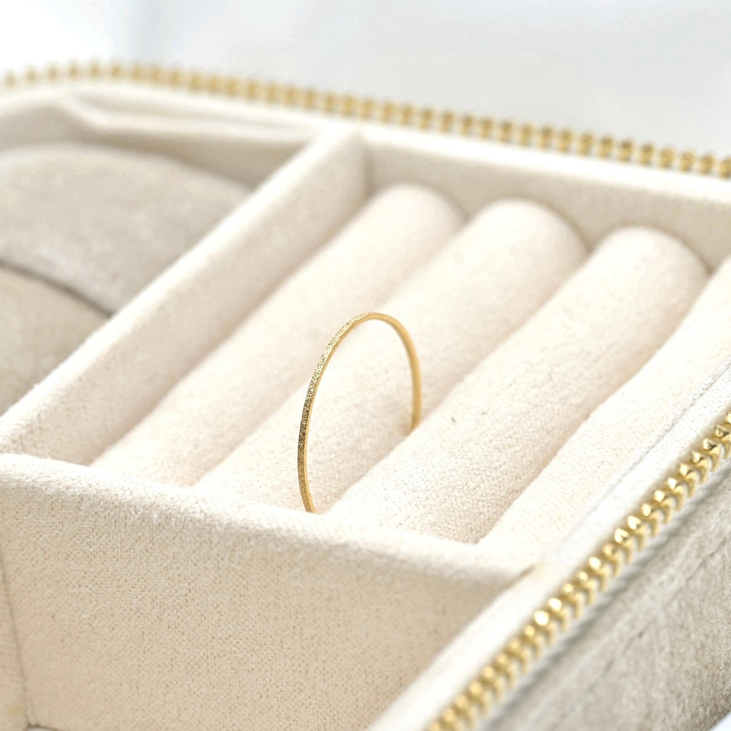 A delicate gold ring with a textured, hammered finish displayed inside a cream-colored velvet jewelry organizer box.