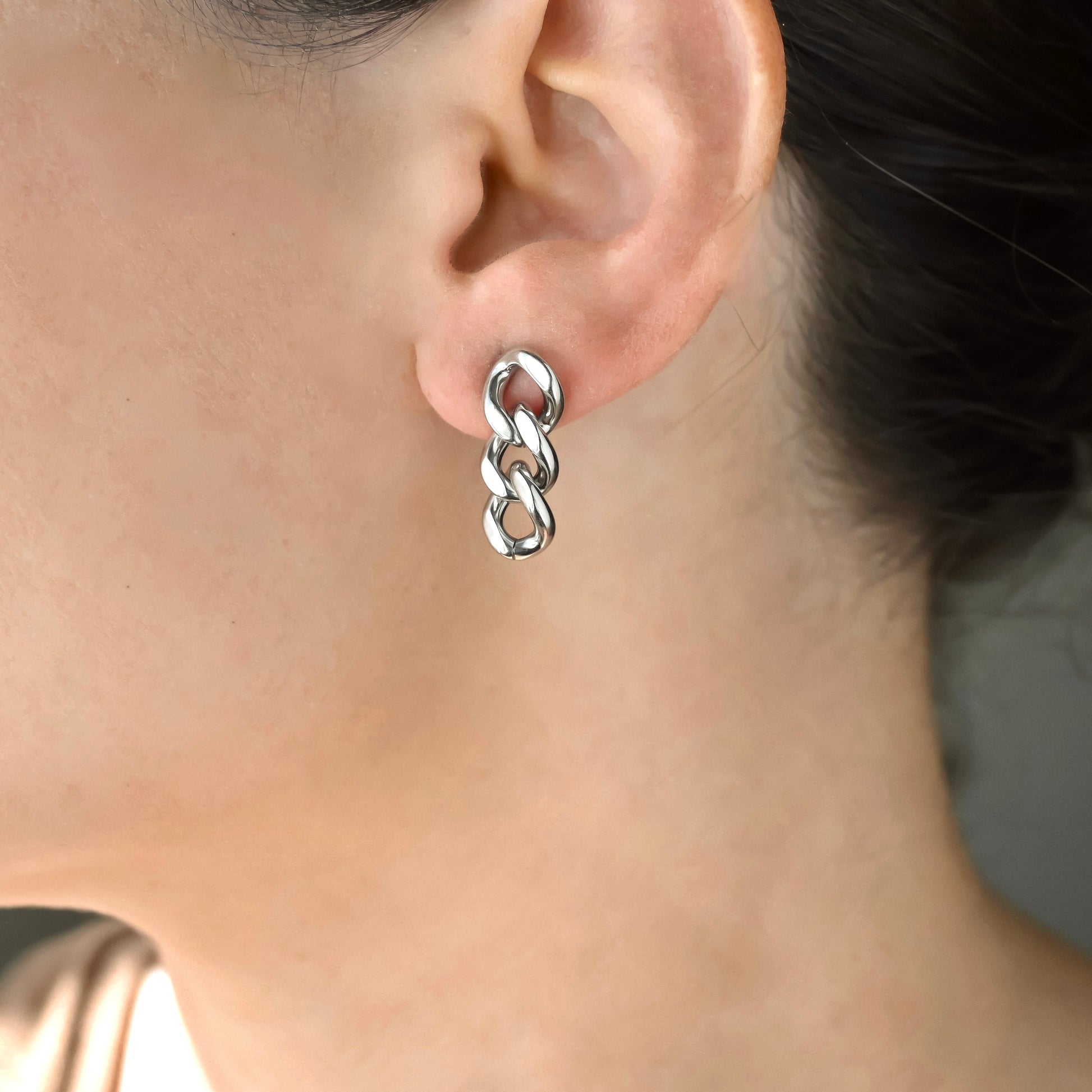 Silver curb link chain earring worn by a person with a neutral background