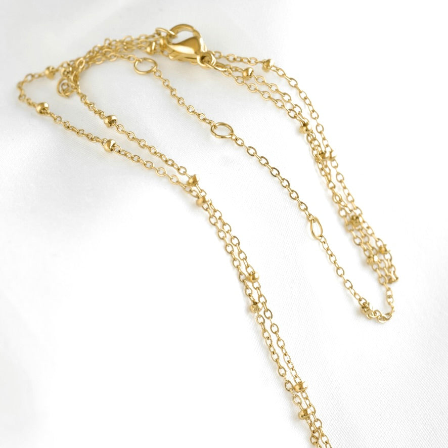 A delicate gold chain necklace with a lobster clasp, displayed on a white textured fabric background.