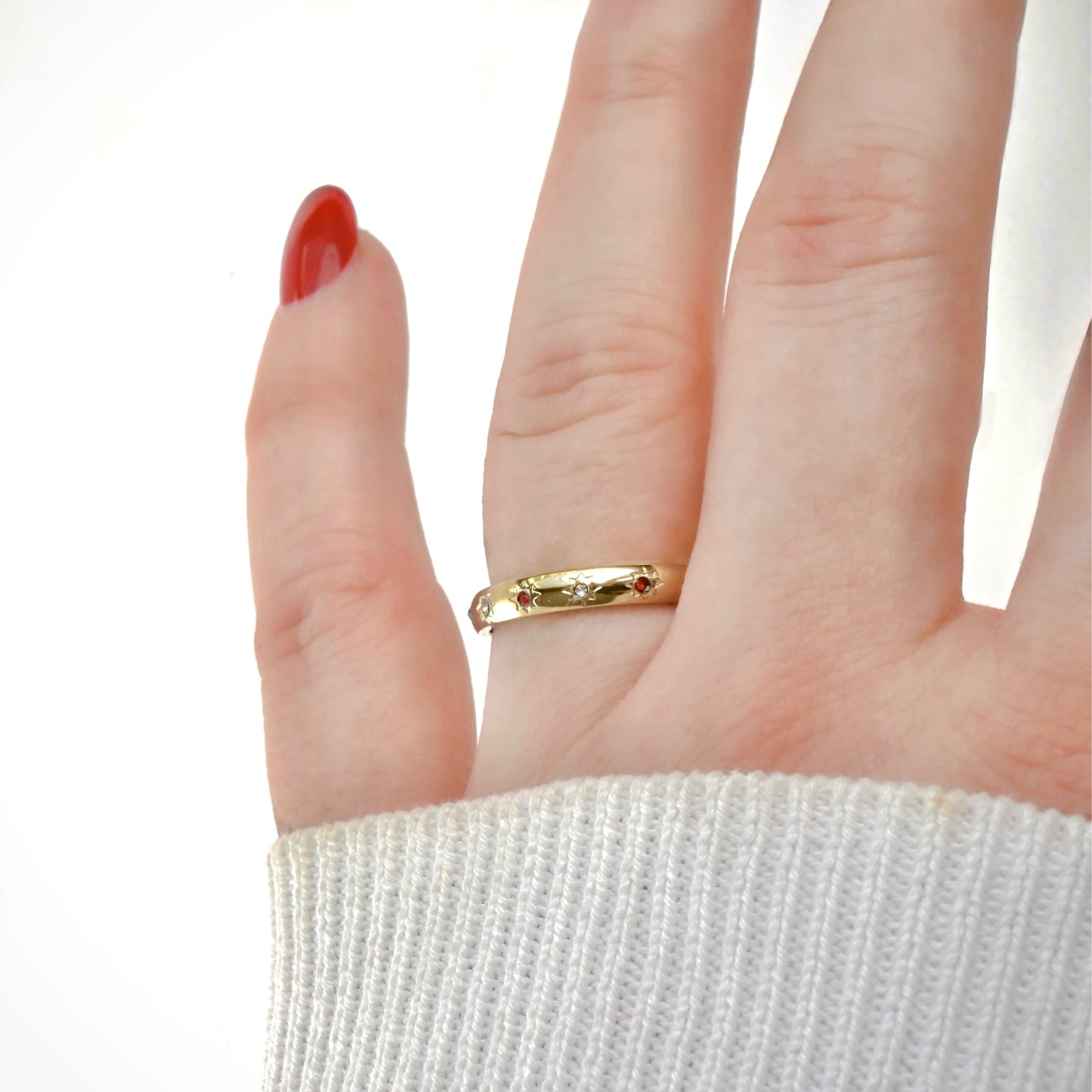 Hand wearing a gold ring with red and clear stones in a star setting with a white background