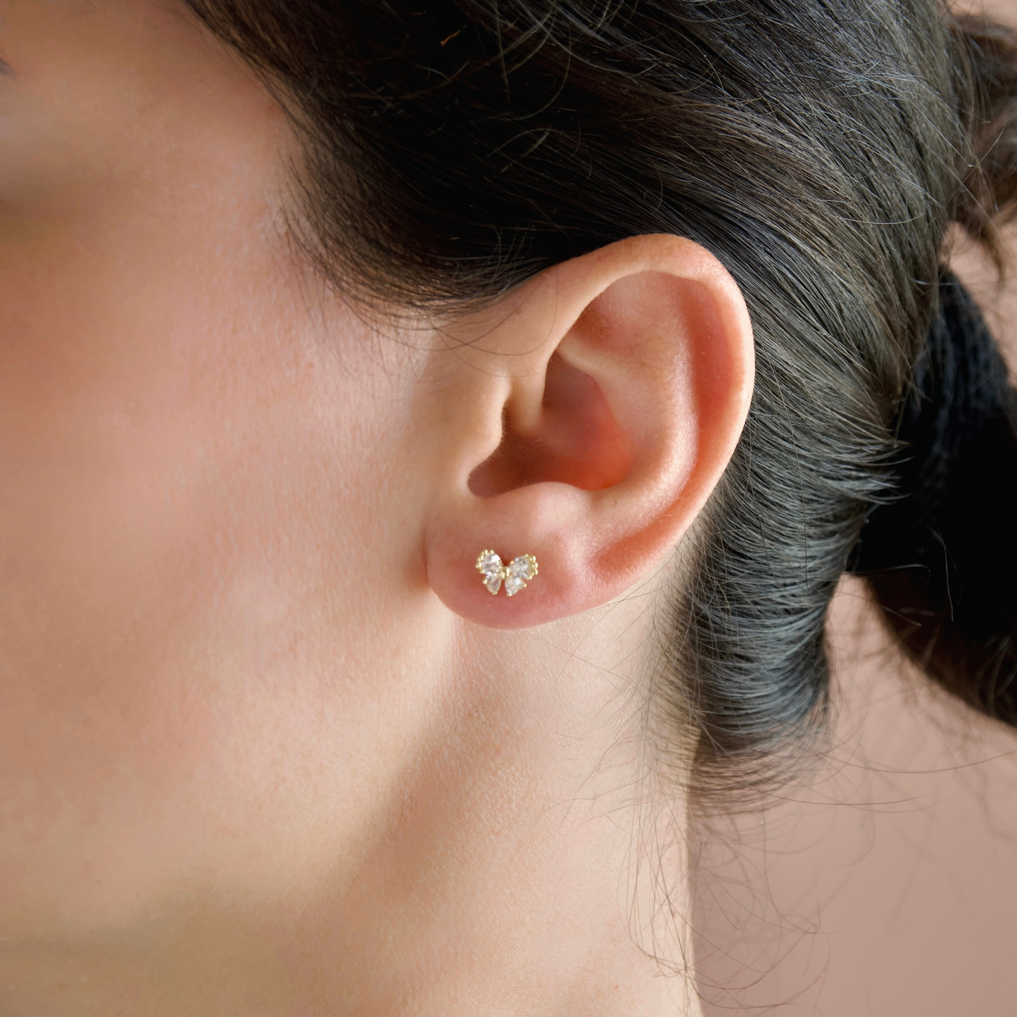 A close-up of a person's ear wearing a small gold butterfly-shaped stud earring with clear stones.